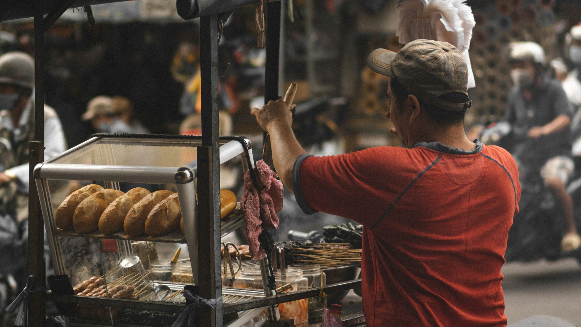 man in red t-shirt and black pants standing in front of food stall during daytime