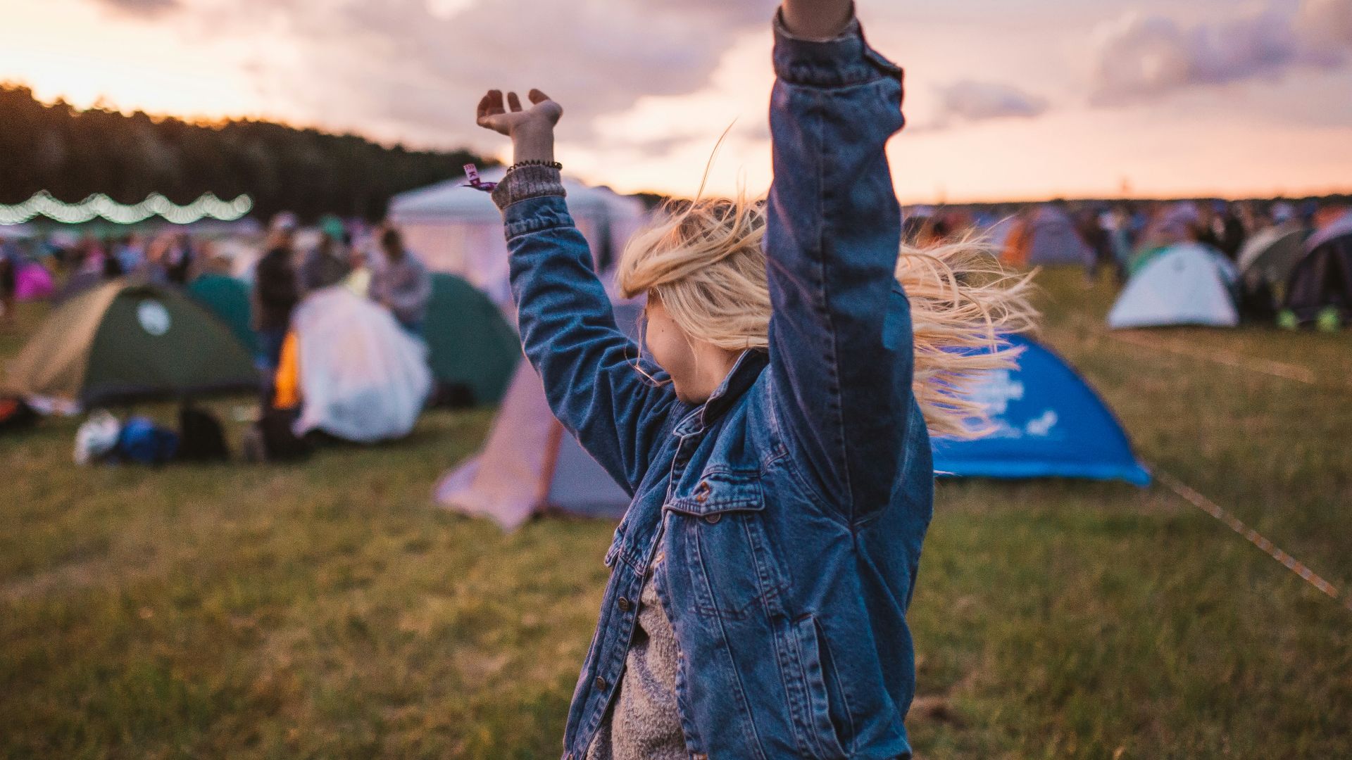 a woman raising her arms in the air in front of tents