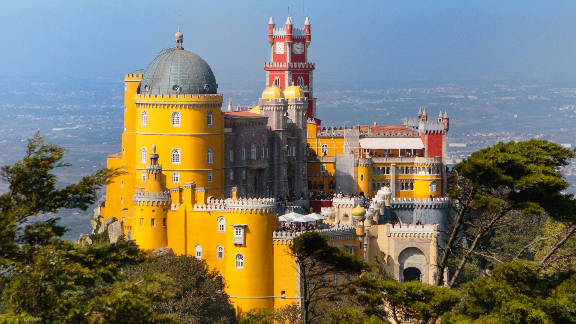 A large yellow castle sitting on top of a lush green hillside