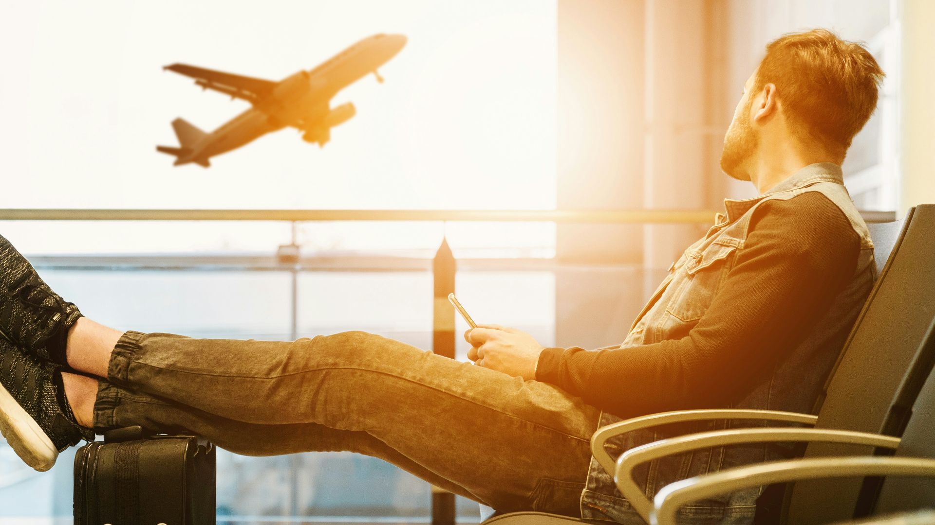 man sitting on gang chair with feet on luggage looking at airplane