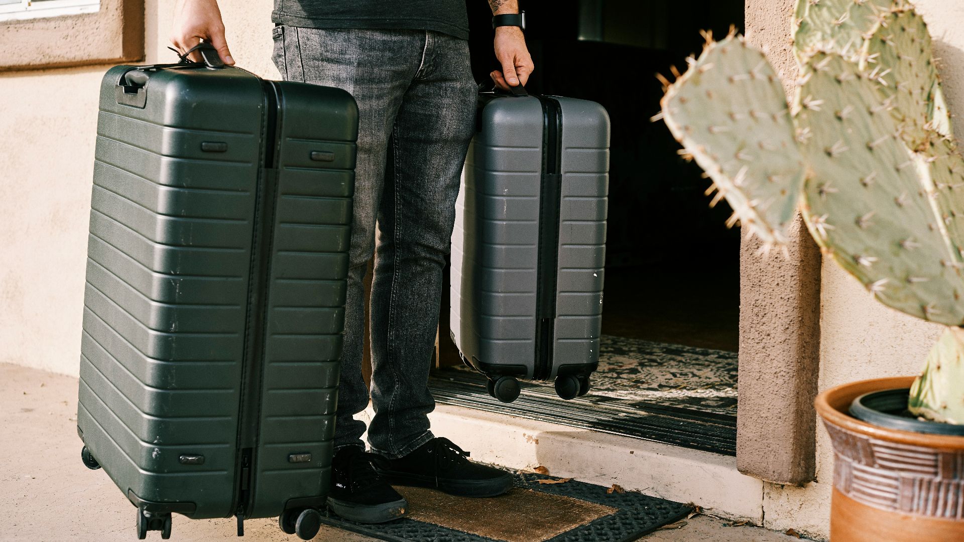 man in black denim jeans and black leather shoes standing beside black luggage bag