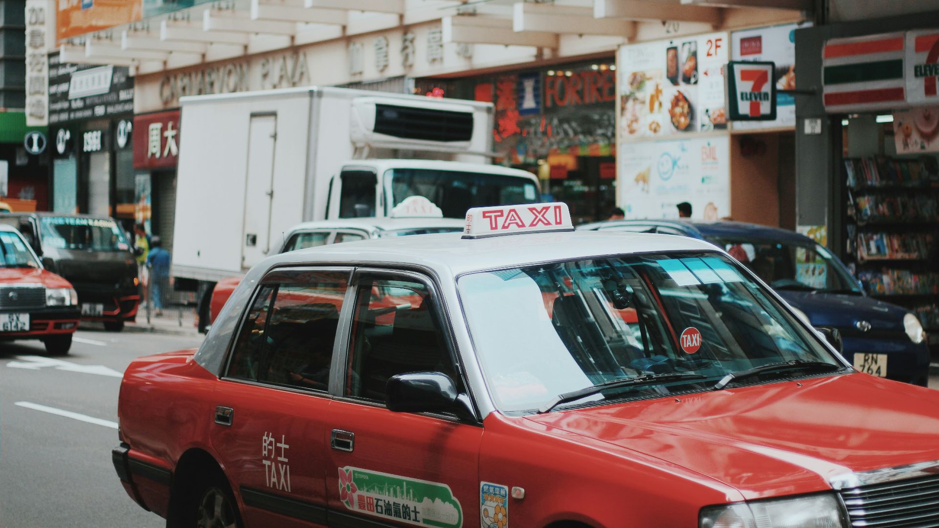 red and white taxi sedan running on road near 7 Eleven store signage