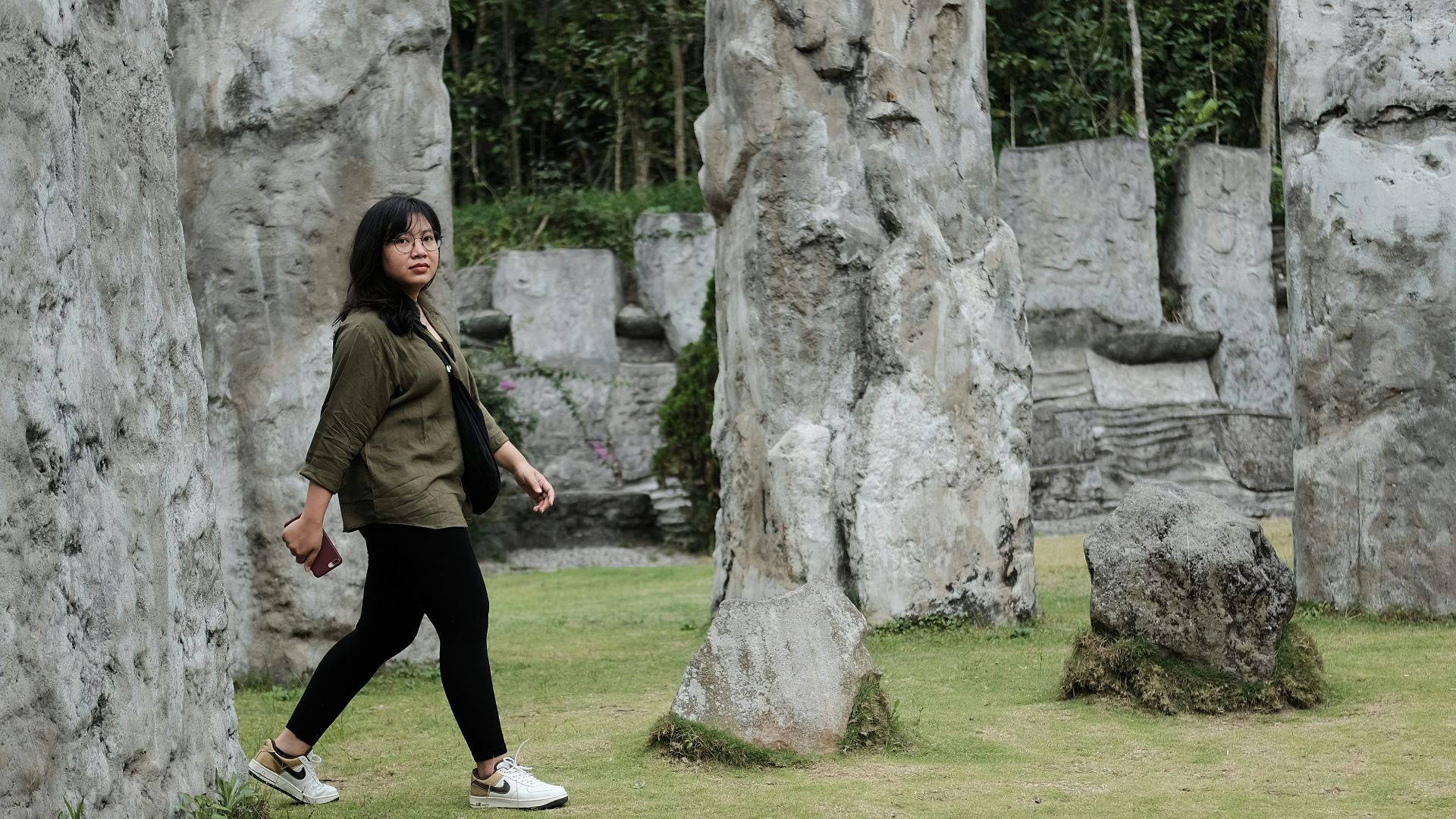 woman in green jacket and black pants standing beside gray rock