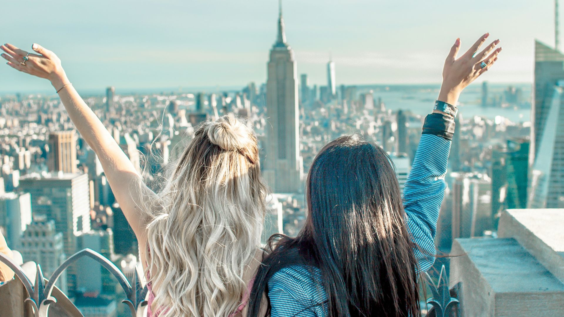 two women hands on their back while raising their hands facing Empire State building
