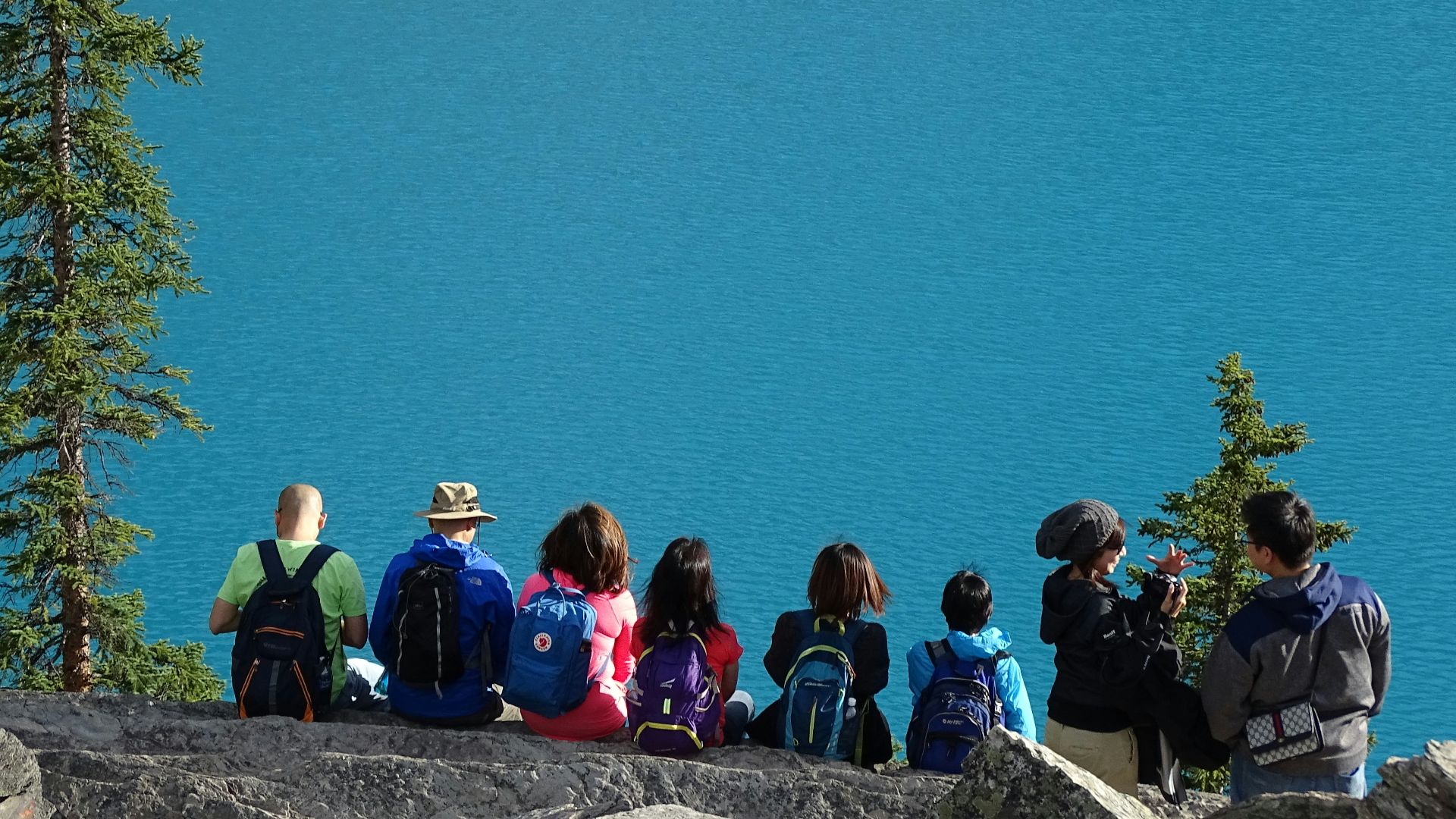 people sitting on rock edge facing body of water