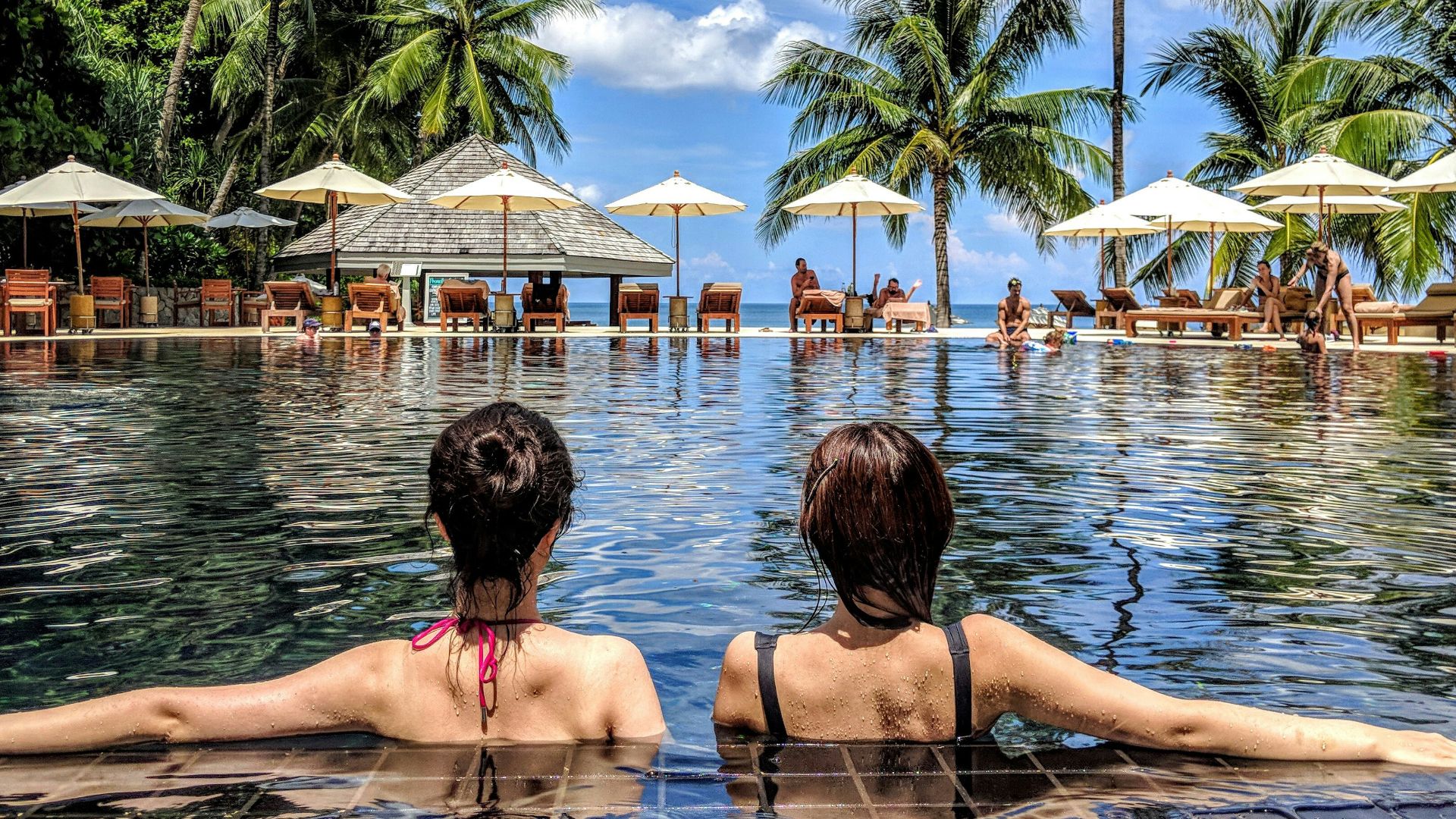 two woman leaning on inground pool tile