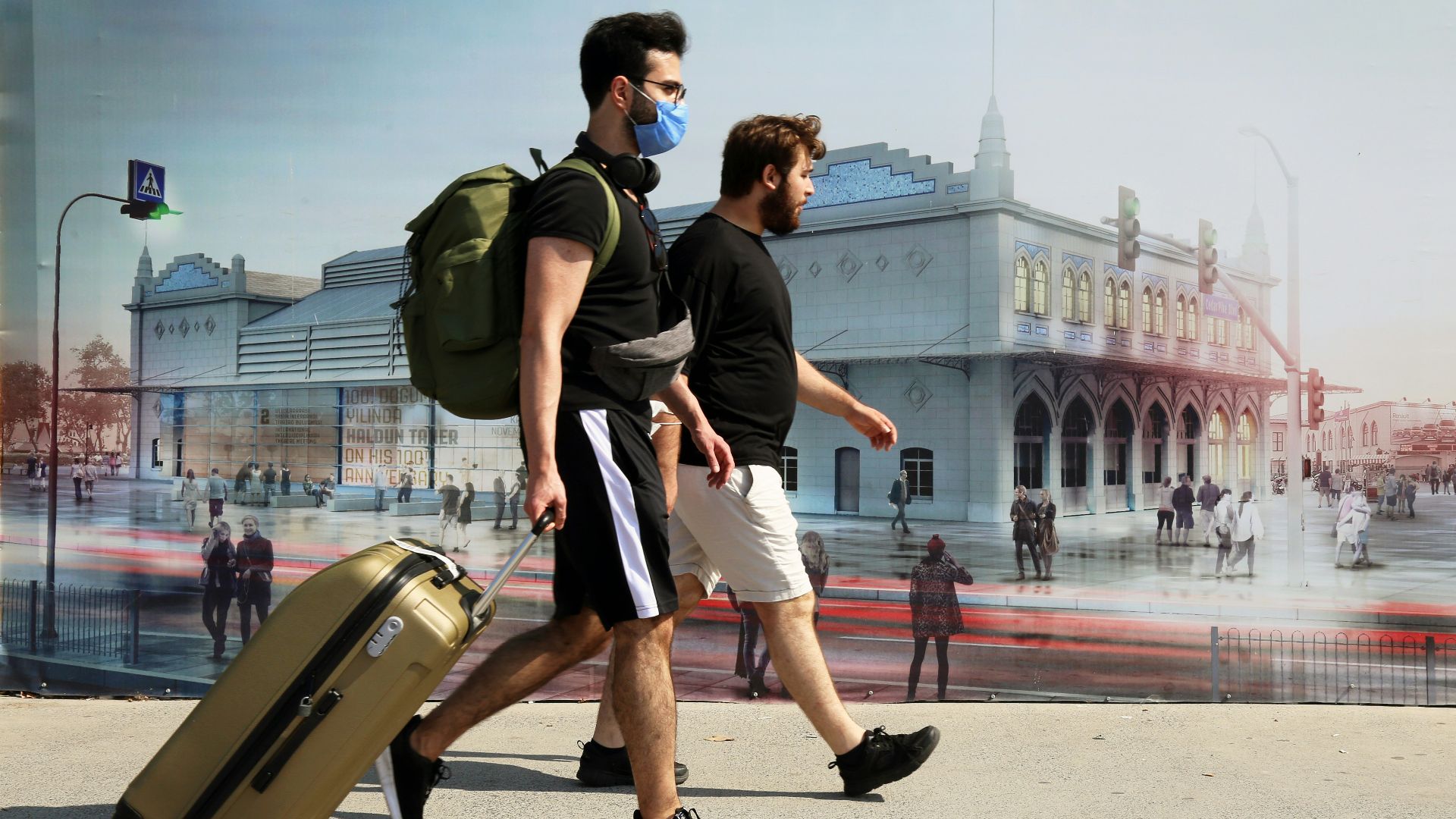 man in black t-shirt and white shorts carrying brown luggage bag walking on street during