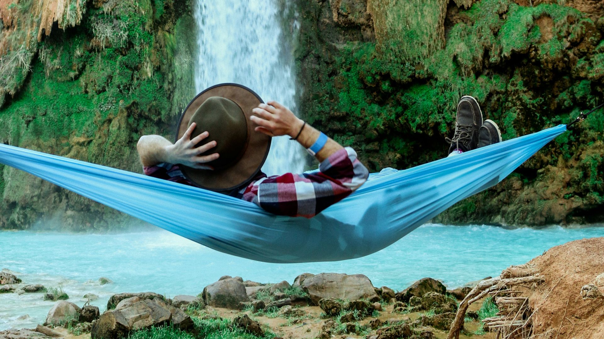 man laying on blue hammock in front of waterfalls