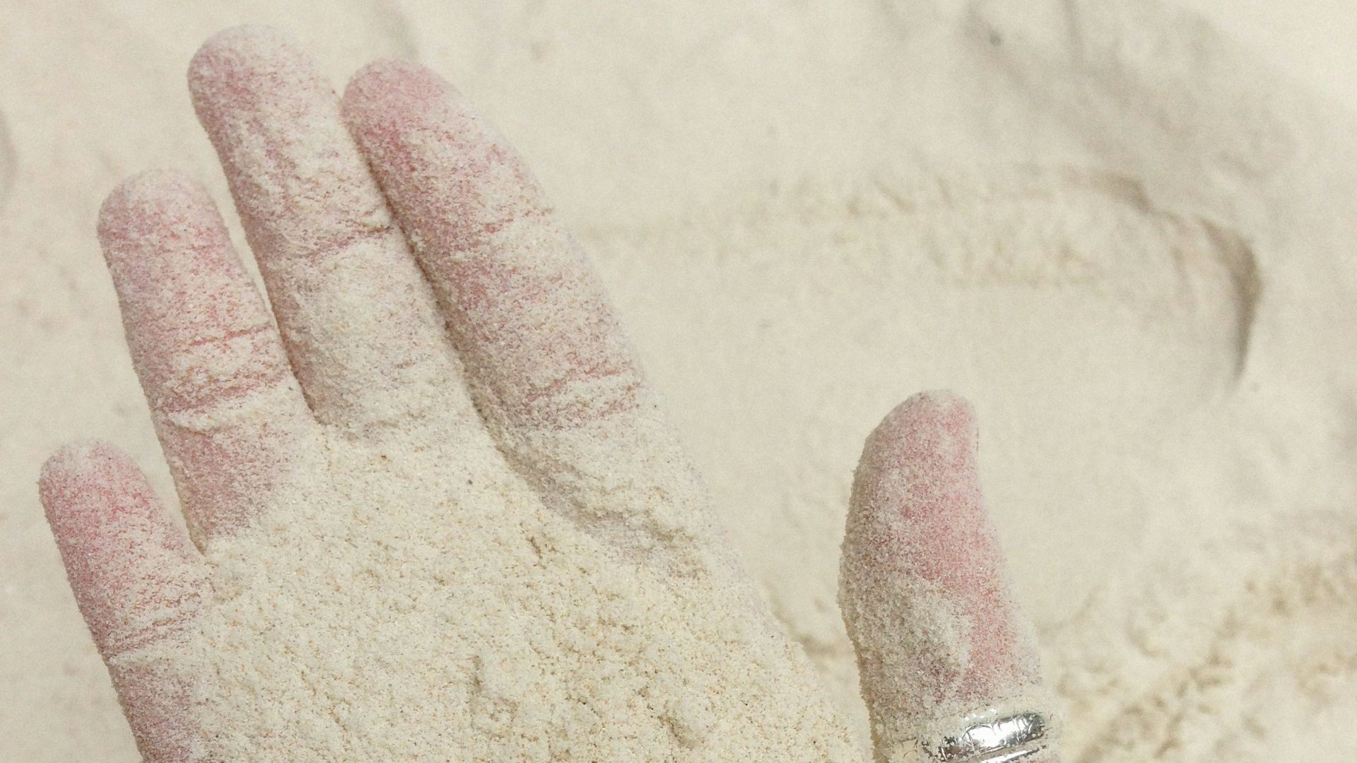 a hand with a ring on it covered in sand