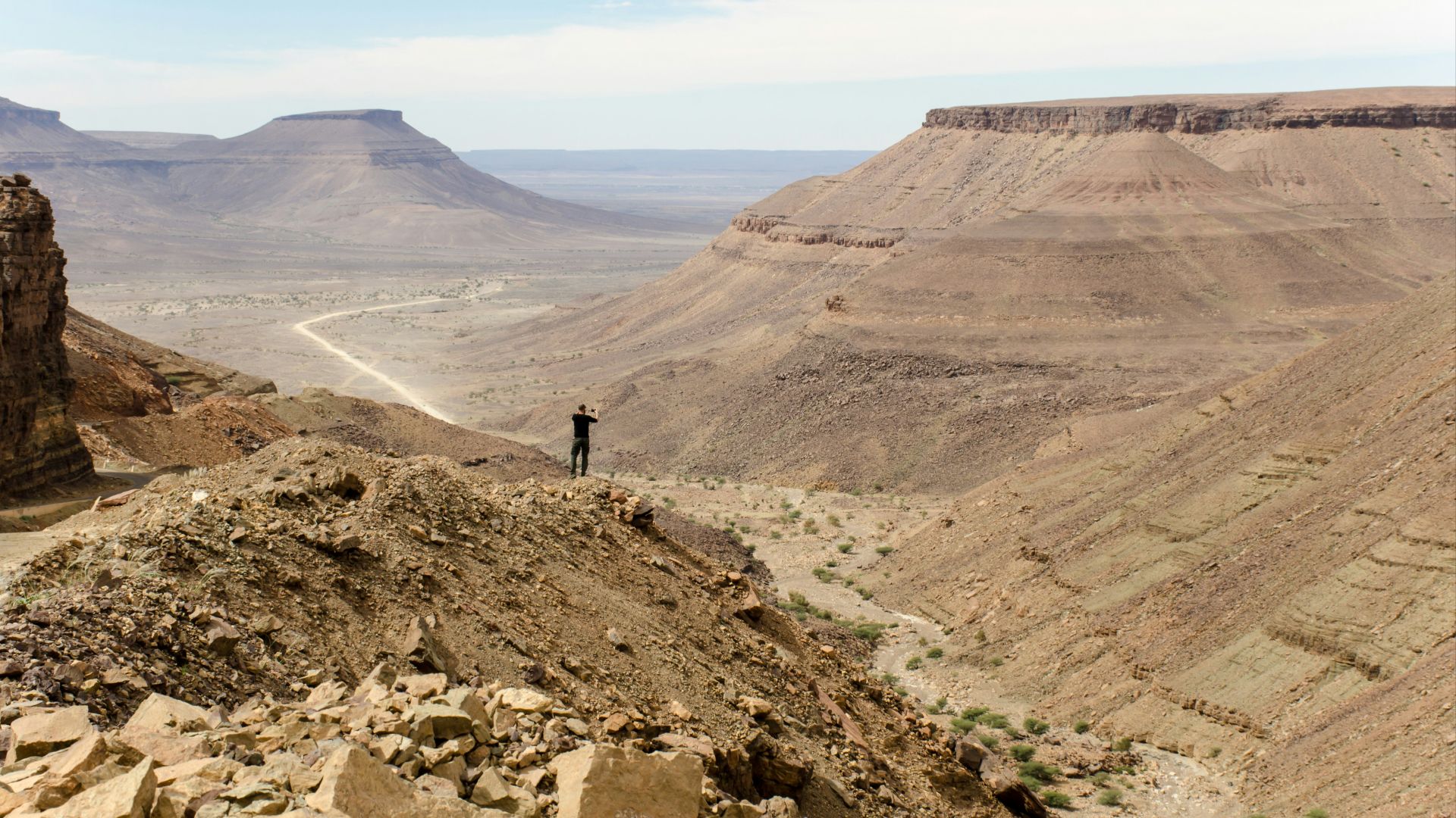 person standing at the edge of a rock mountain facing the mountains during day
