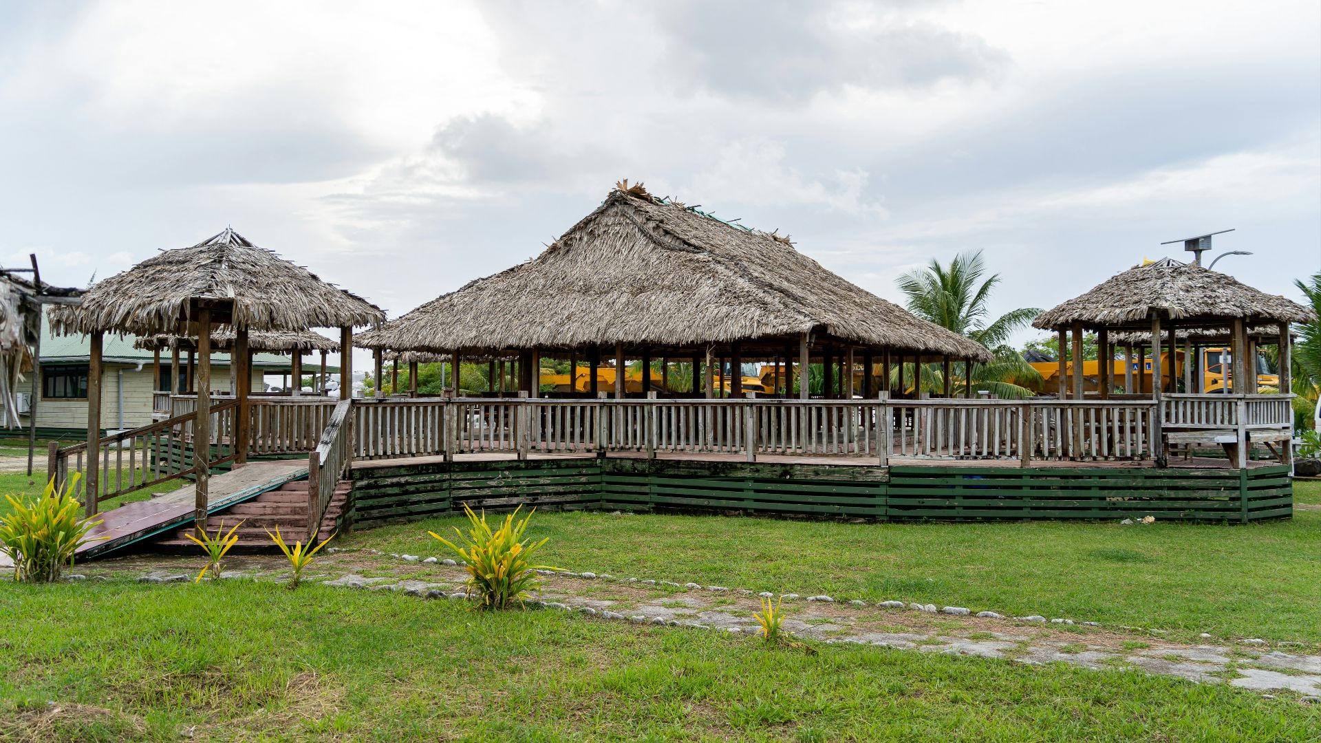 A grassy area with a wooden walkway and thatched huts