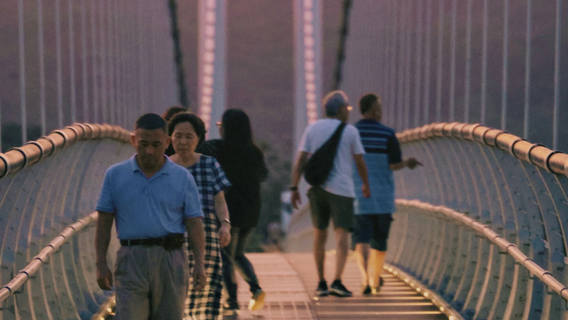 People walk across a suspension bridge at sunset.