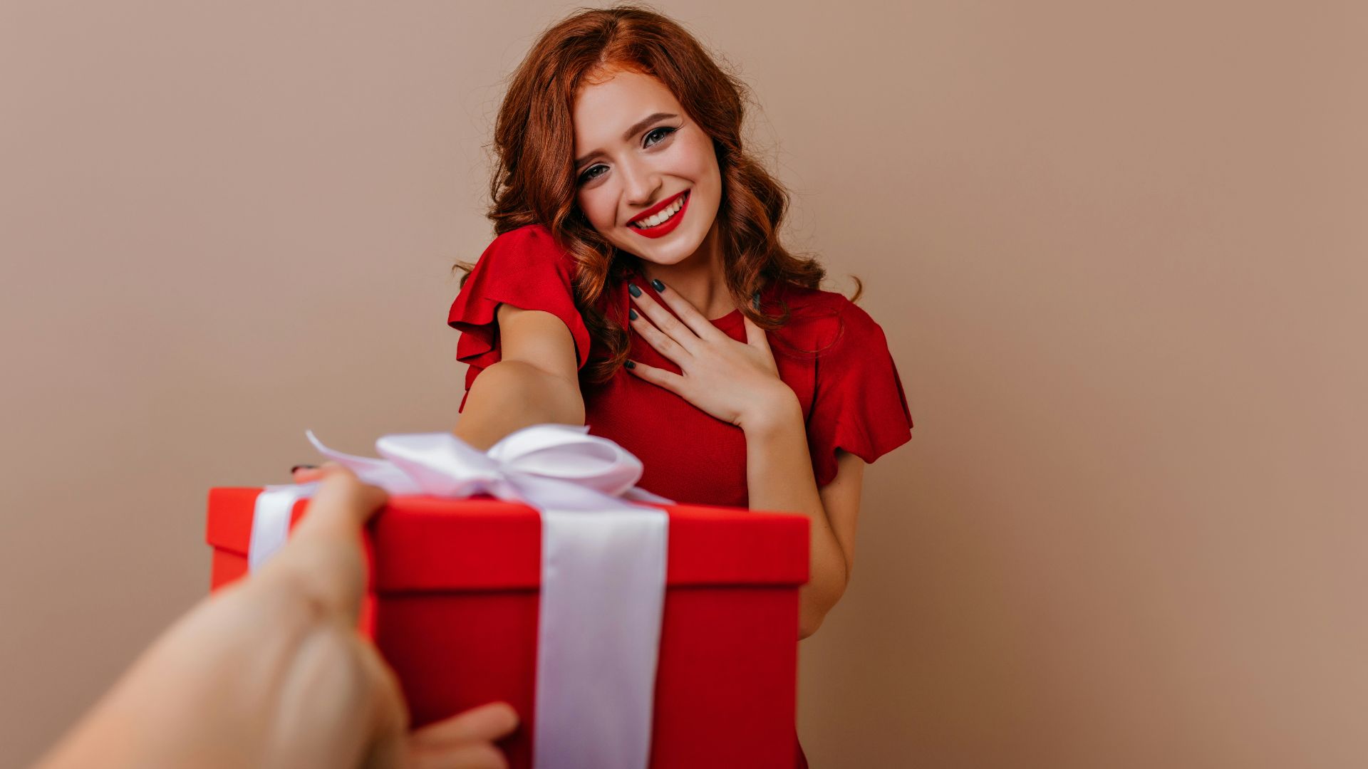 a woman holding a red gift box with a white ribbon