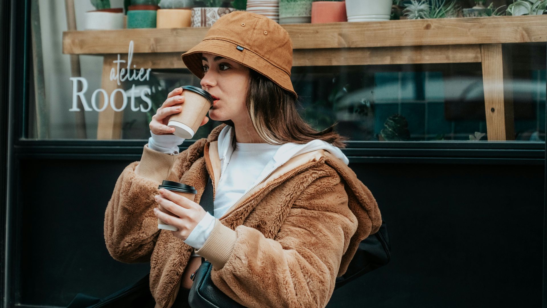 woman in brown coat holding white ceramic mug