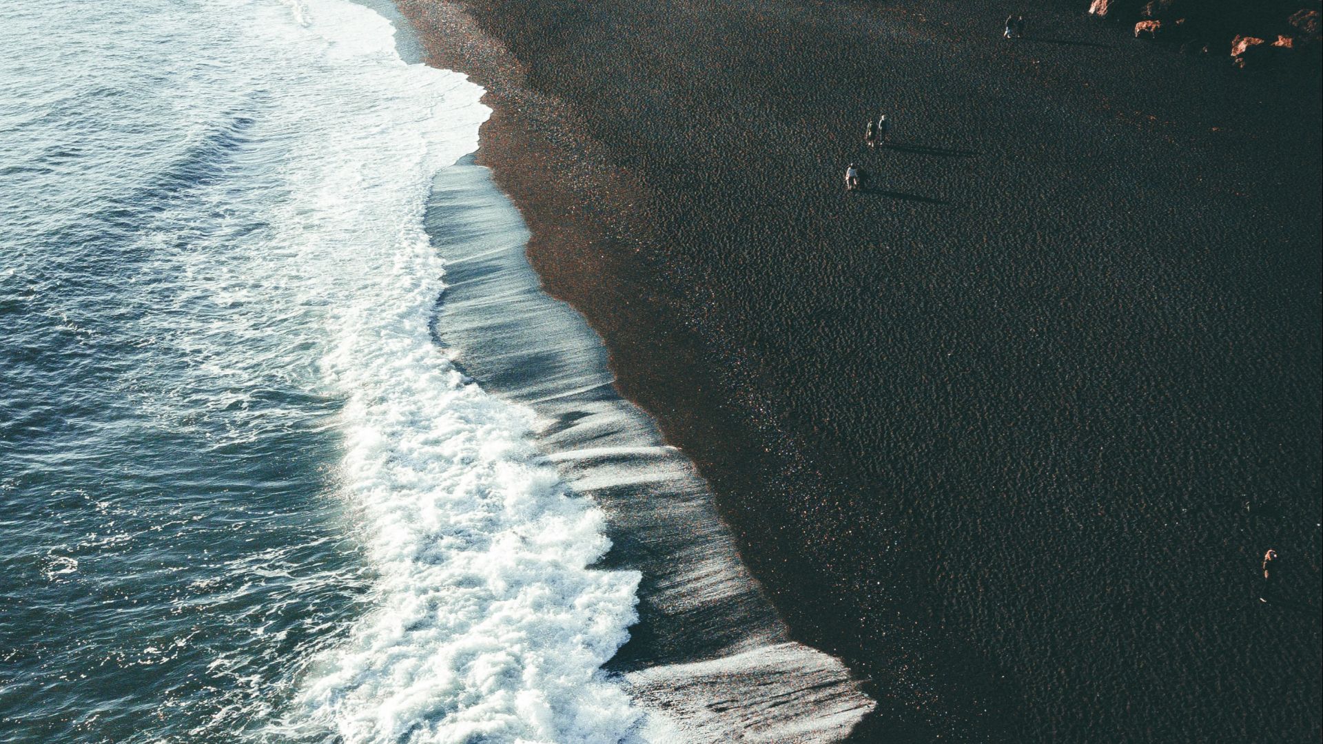 a black beach with waves coming in to the shore
