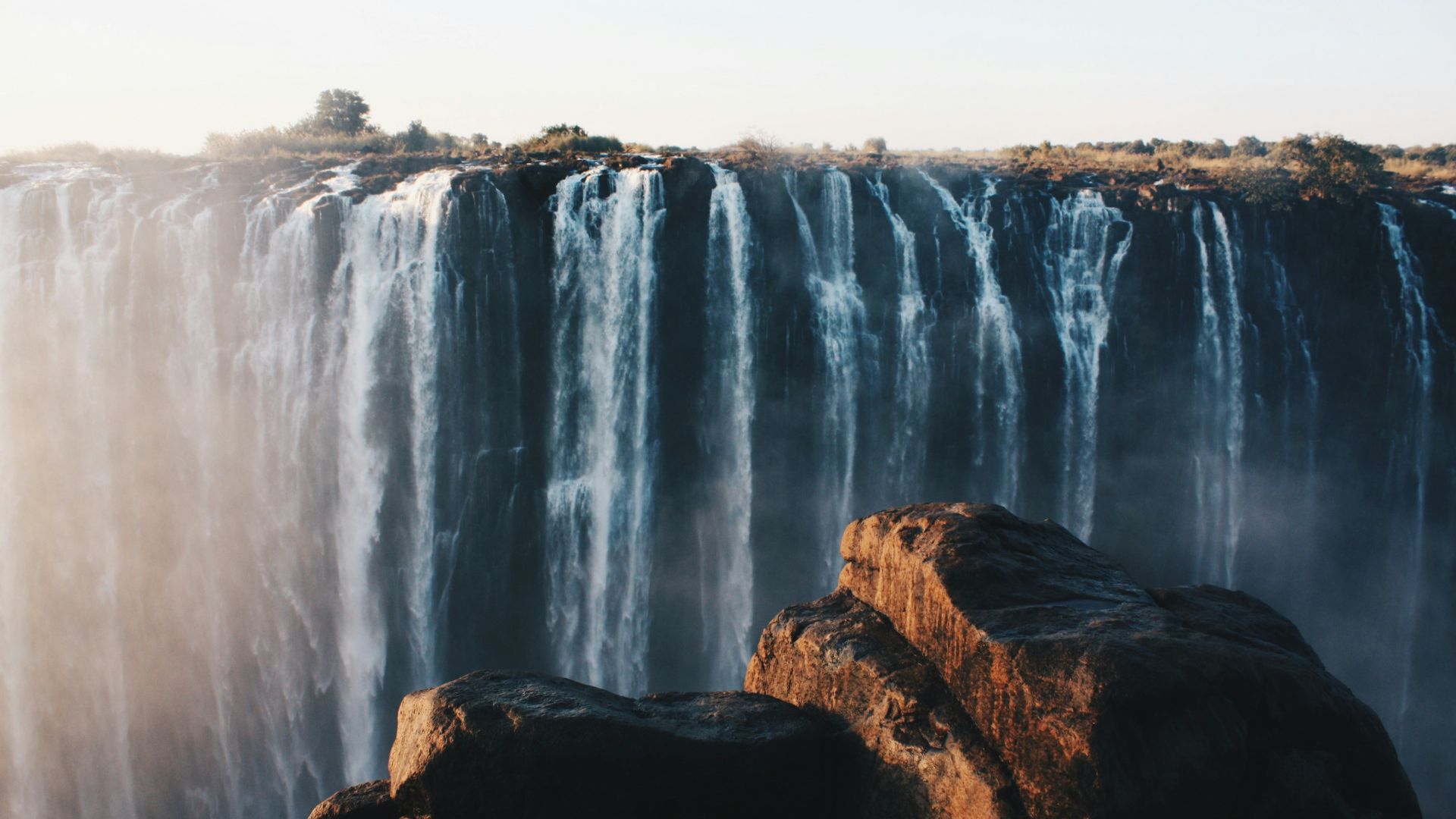 water falls on brown rocky mountain during daytime