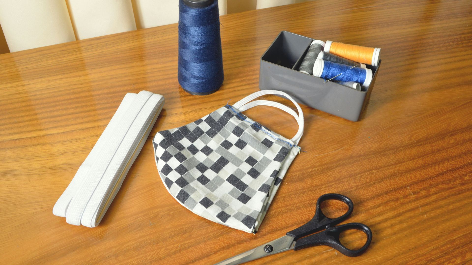 black handled scissors beside blue thread and white and black checkered pouch