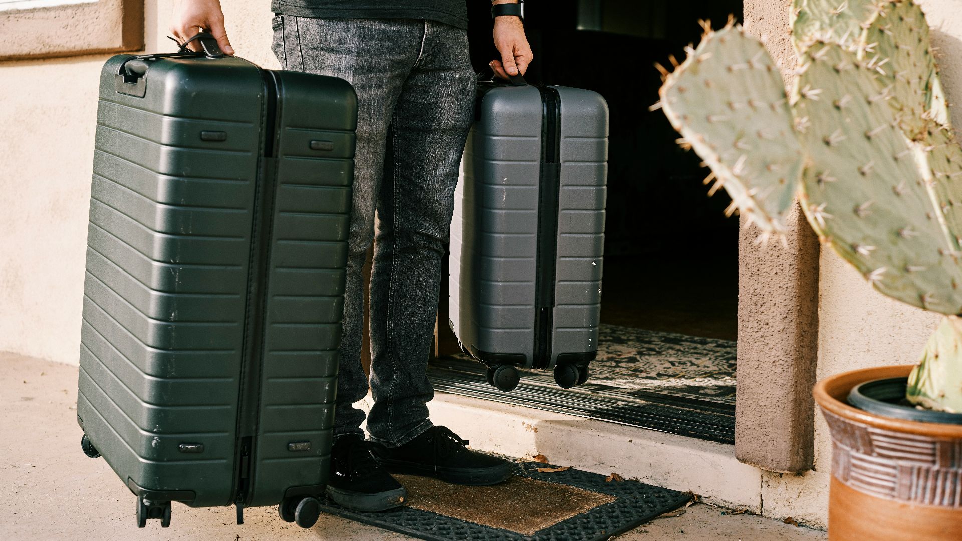 man in black denim jeans and black leather shoes standing beside black luggage bag