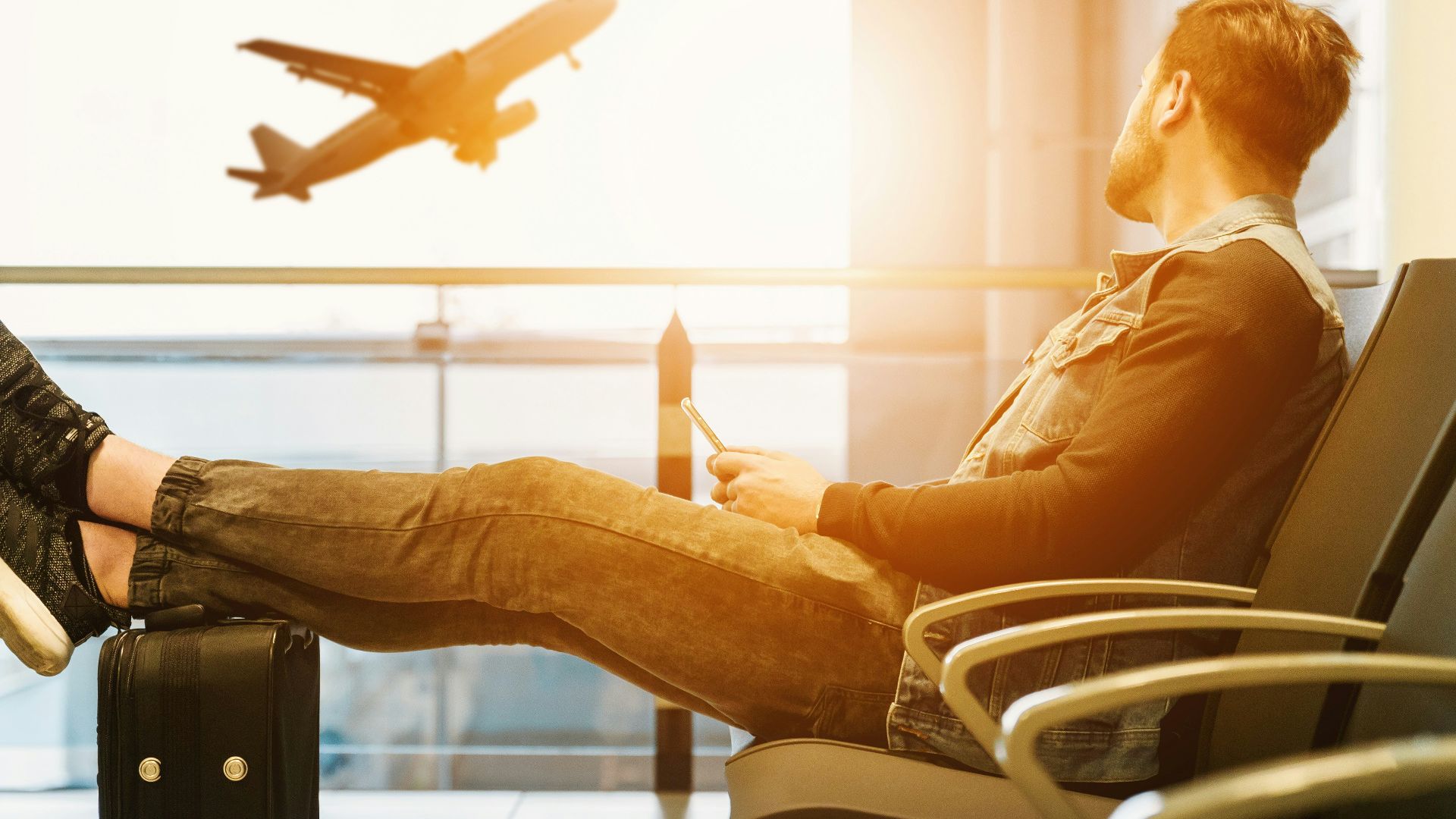 man sitting on gang chair with feet on luggage looking at airplane