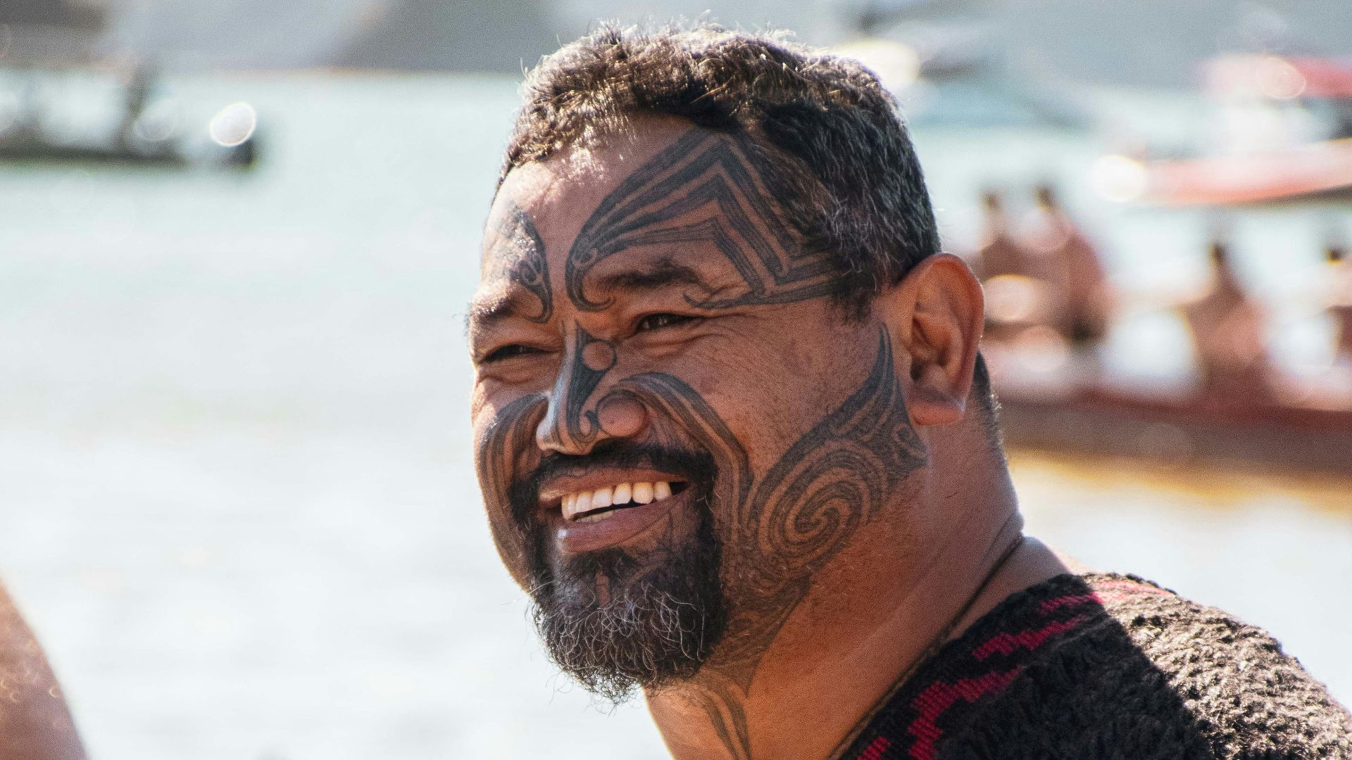 a man with a beard and tattoos standing next to a body of water