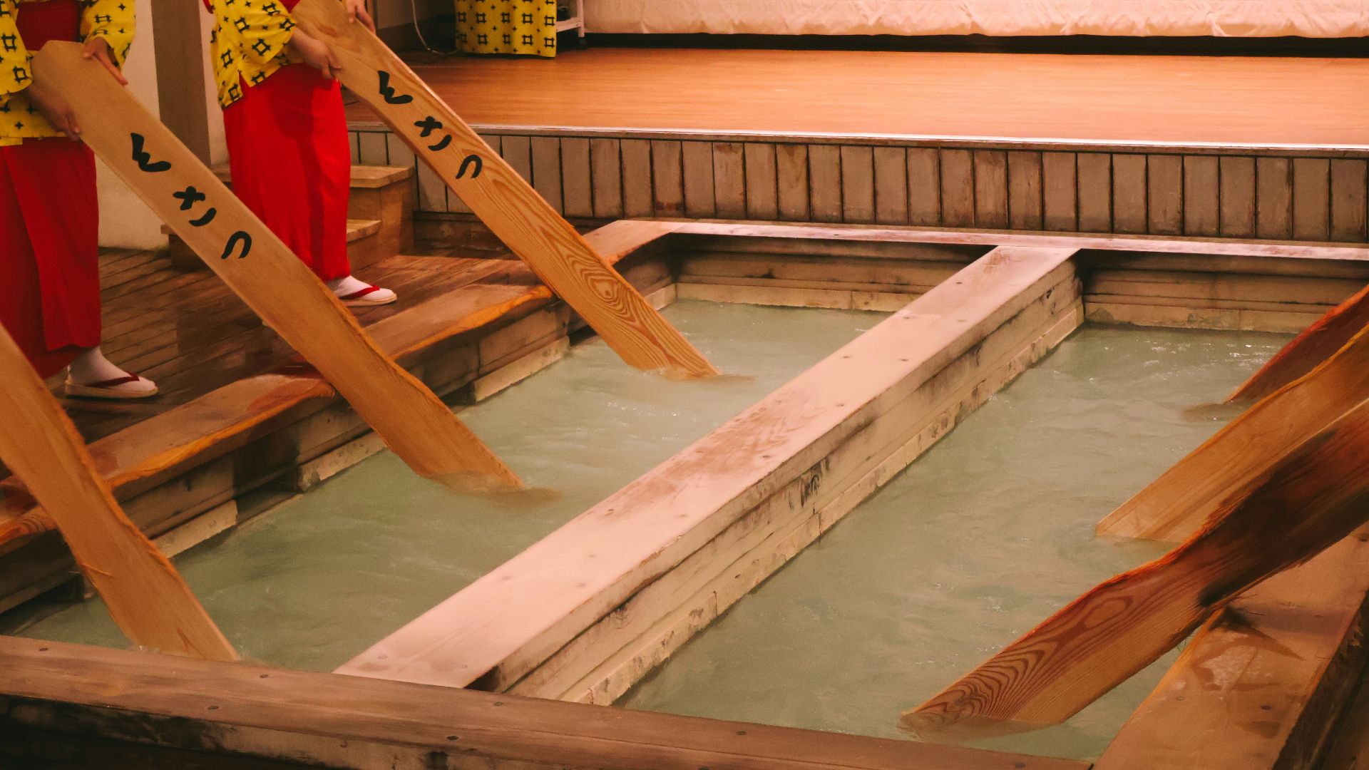 People stir hot spring water with wooden paddles.