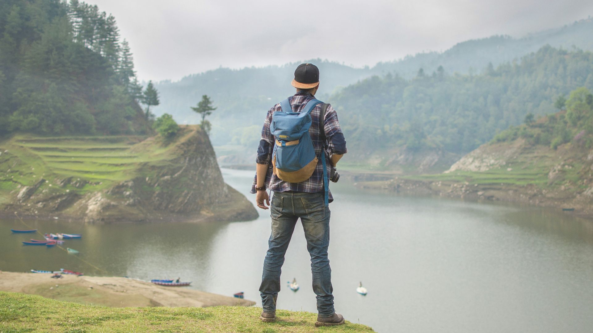 person in blue denim pants carrying blue backpack in front of body of water during daytime