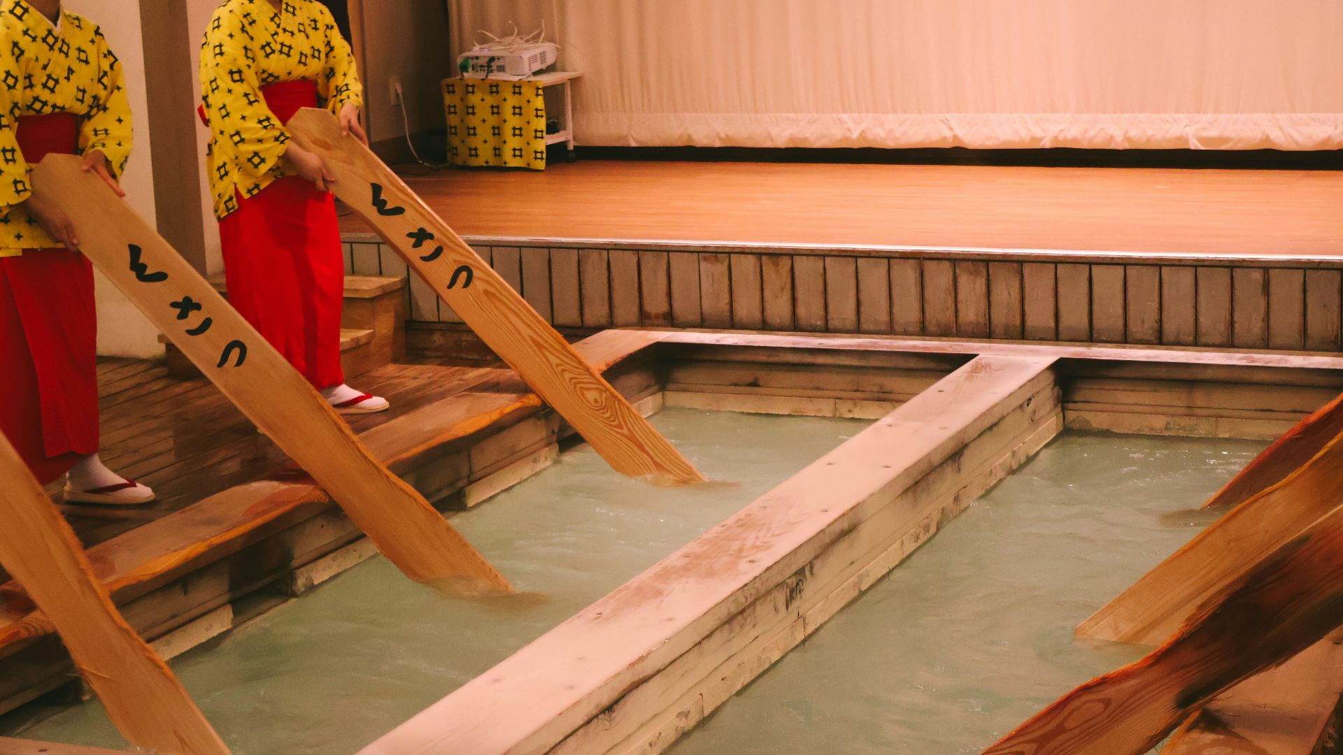 People stir hot spring water with wooden paddles.