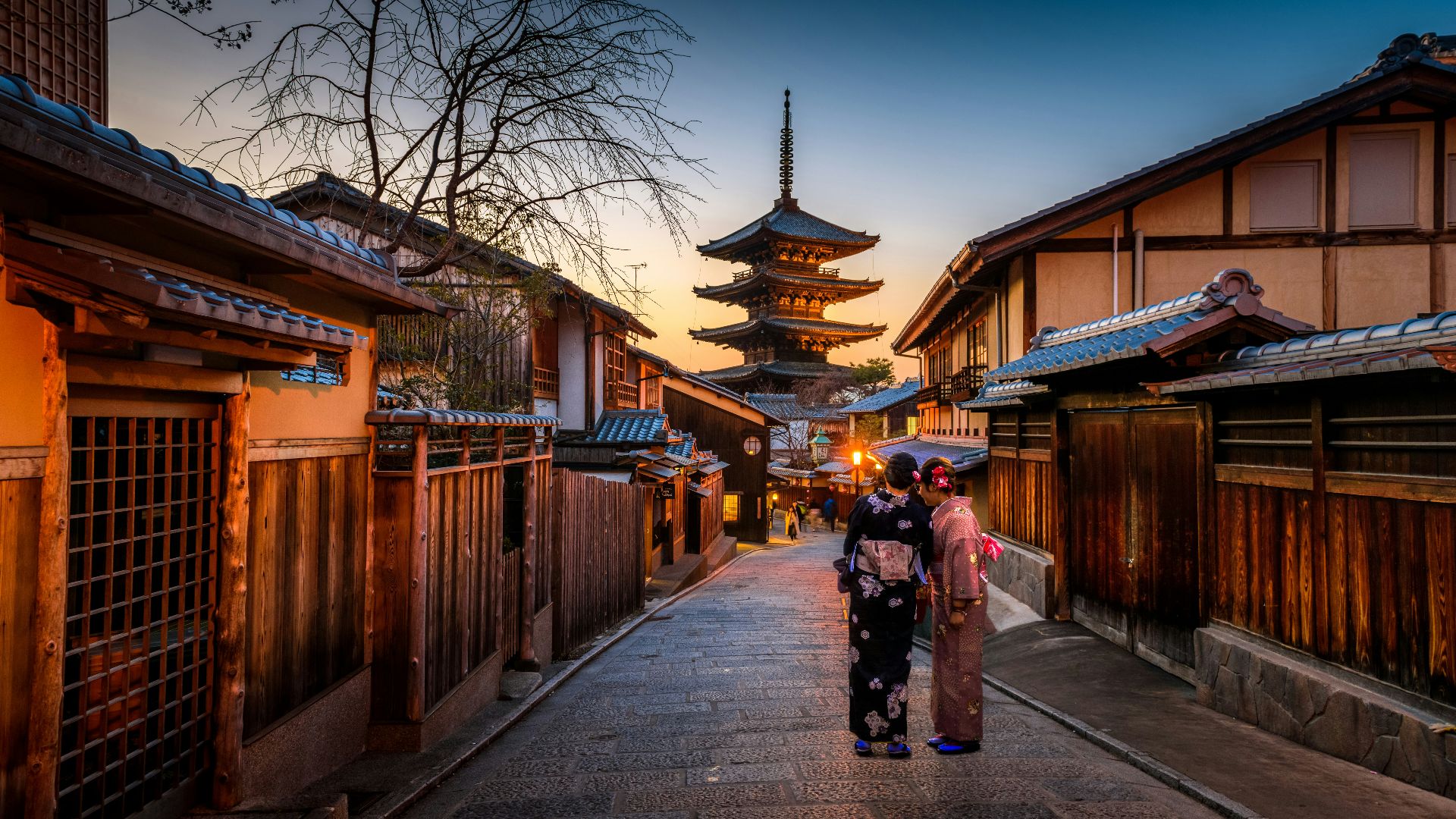 two women in purple and pink kimono standing on street