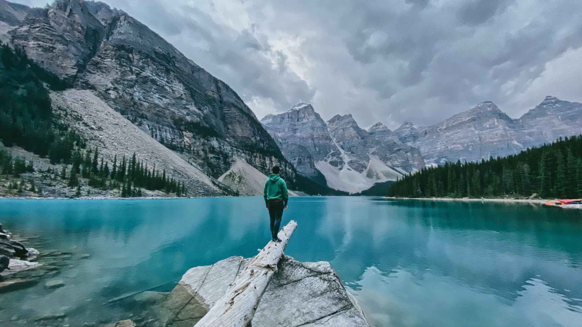 person in green jacket and black pants standing on rock near lake during daytime