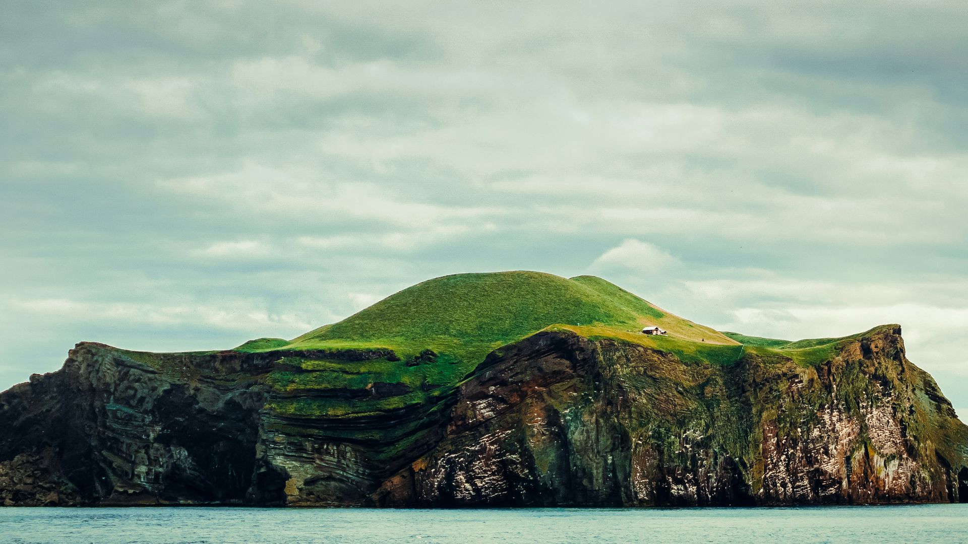 green and brown mountain beside body of water under cloudy sky during daytime
