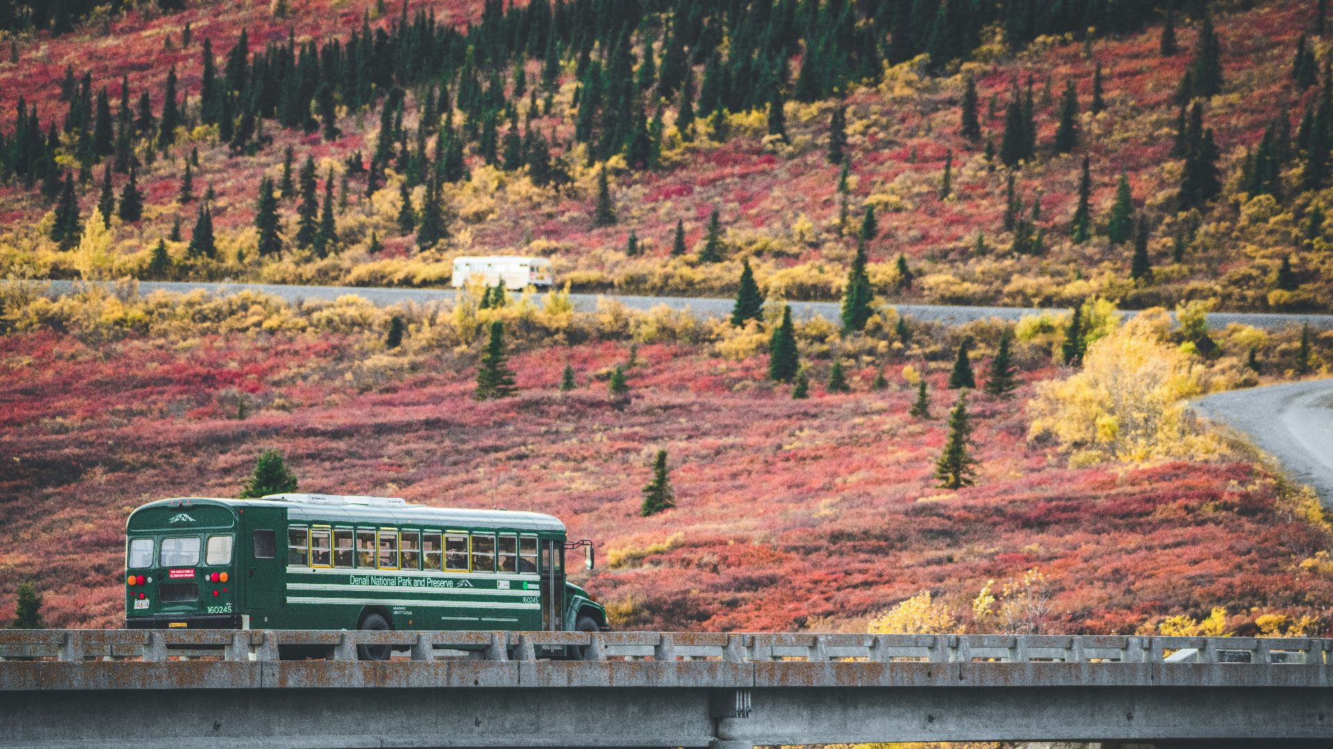 a green bus driving over a bridge in the mountains