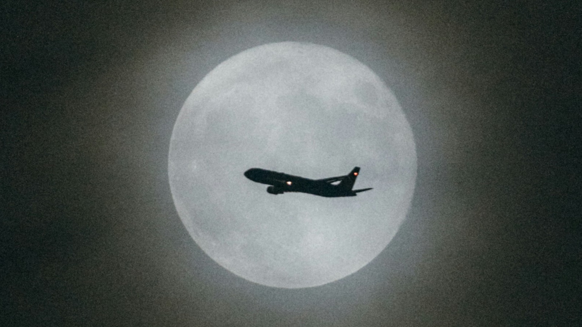 an airplane flying in the sky with the moon in the background