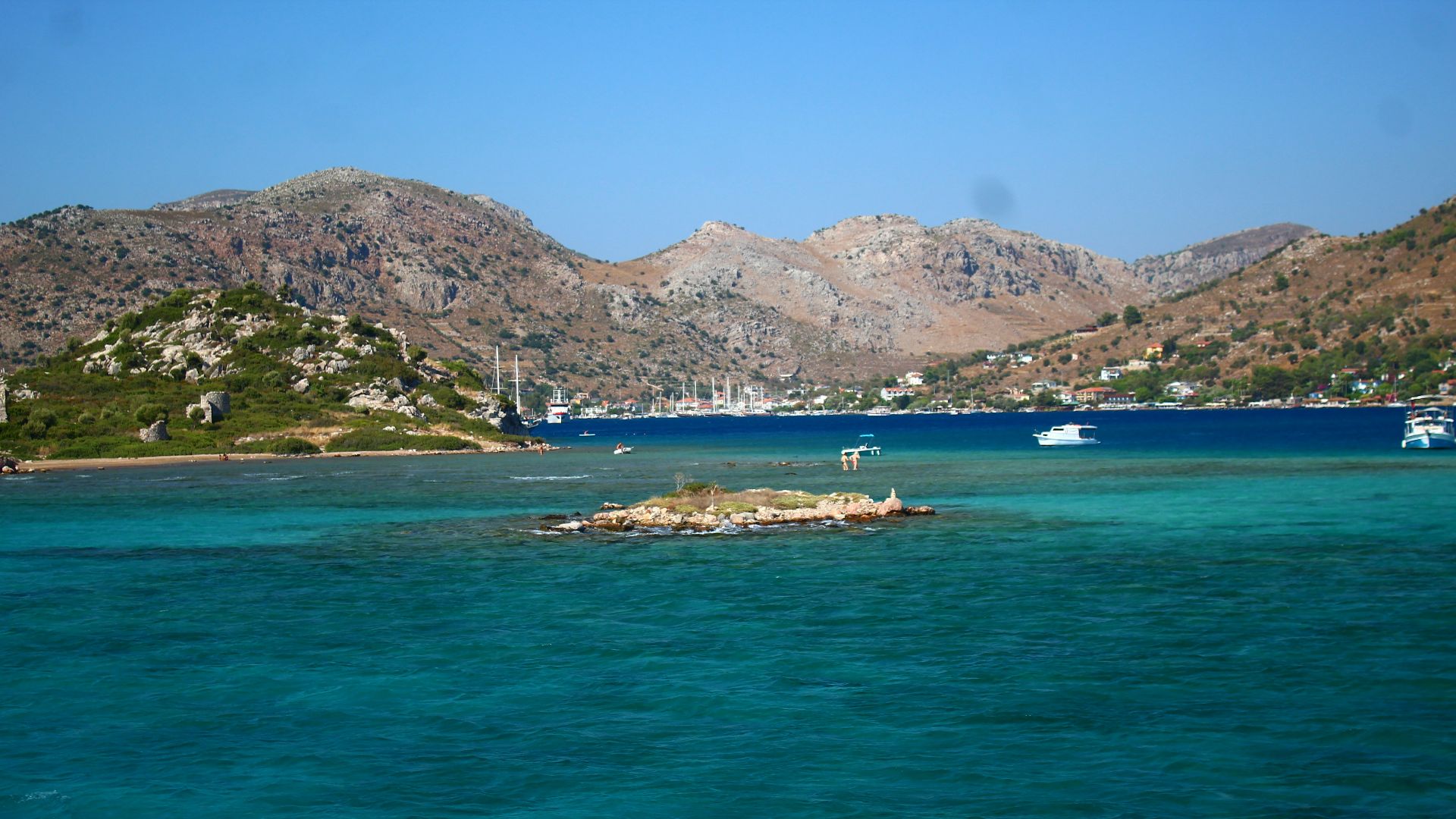 Boats sail on turquoise water near rocky hills.