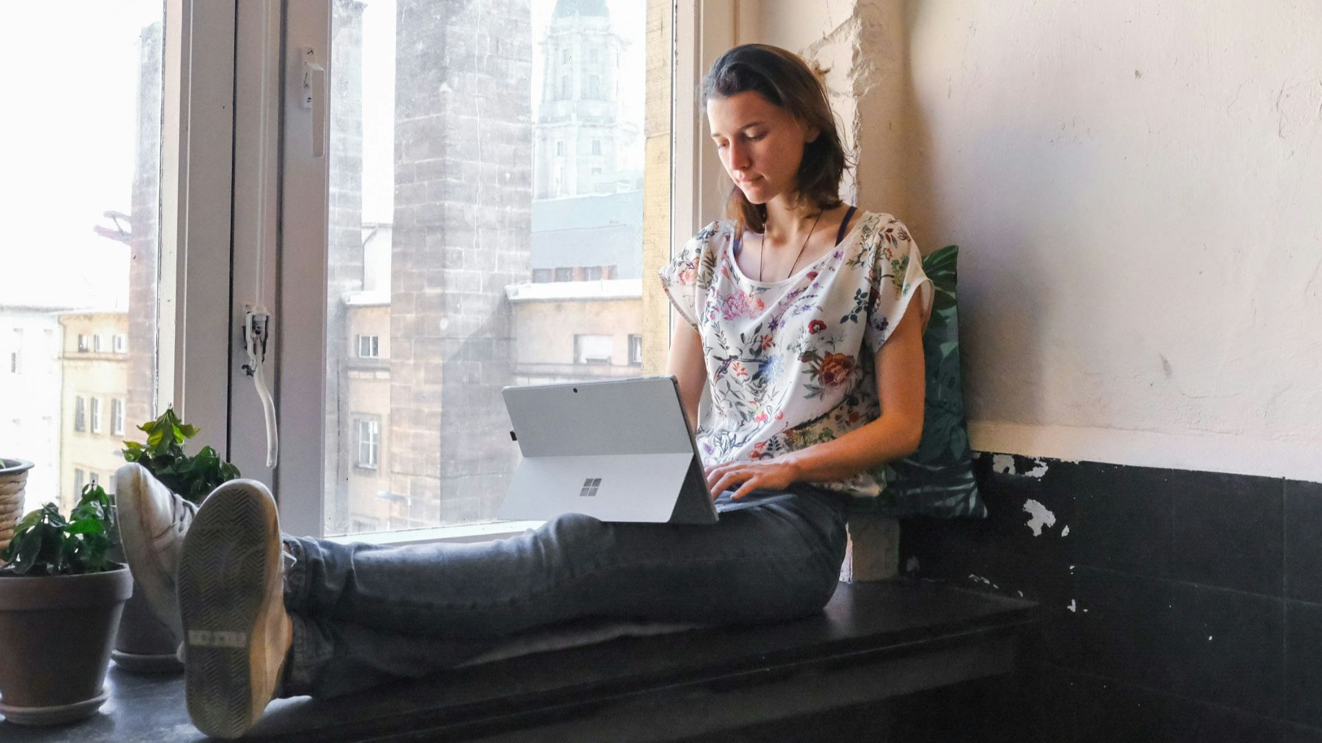 woman wearing white and red floral top sitting besides window