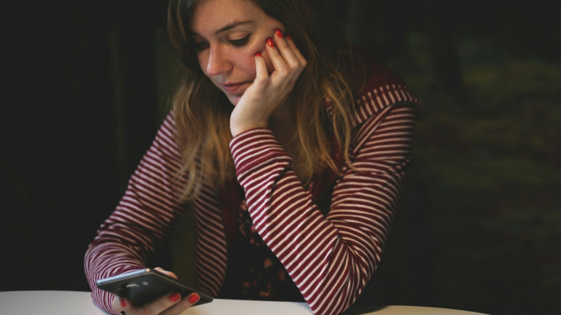 woman leaning on white wooden table while holding black Android smartphone