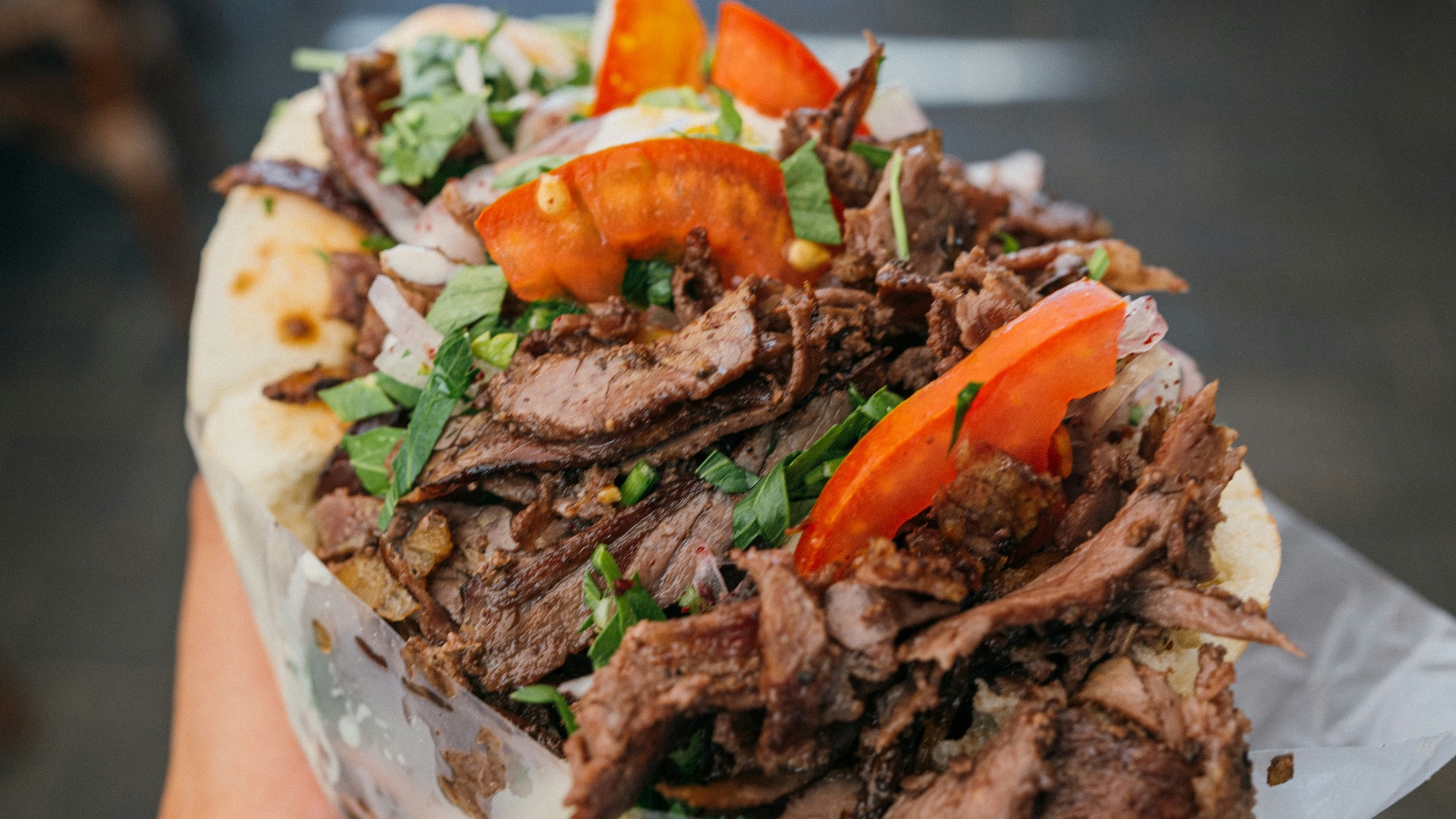 a person holding a sandwich with meat and vegetables