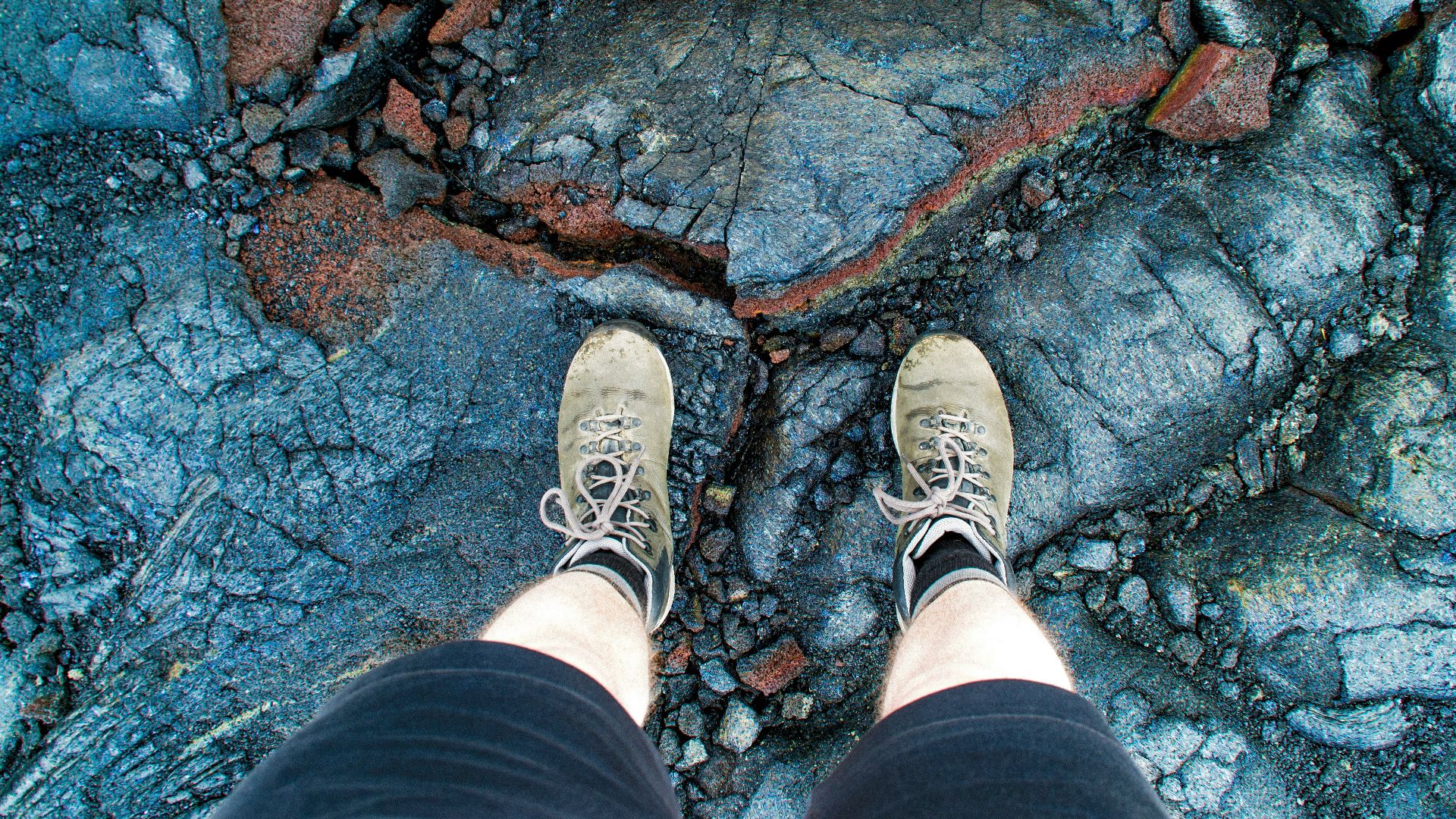person in black shorts and white sneakers standing on rocky ground
