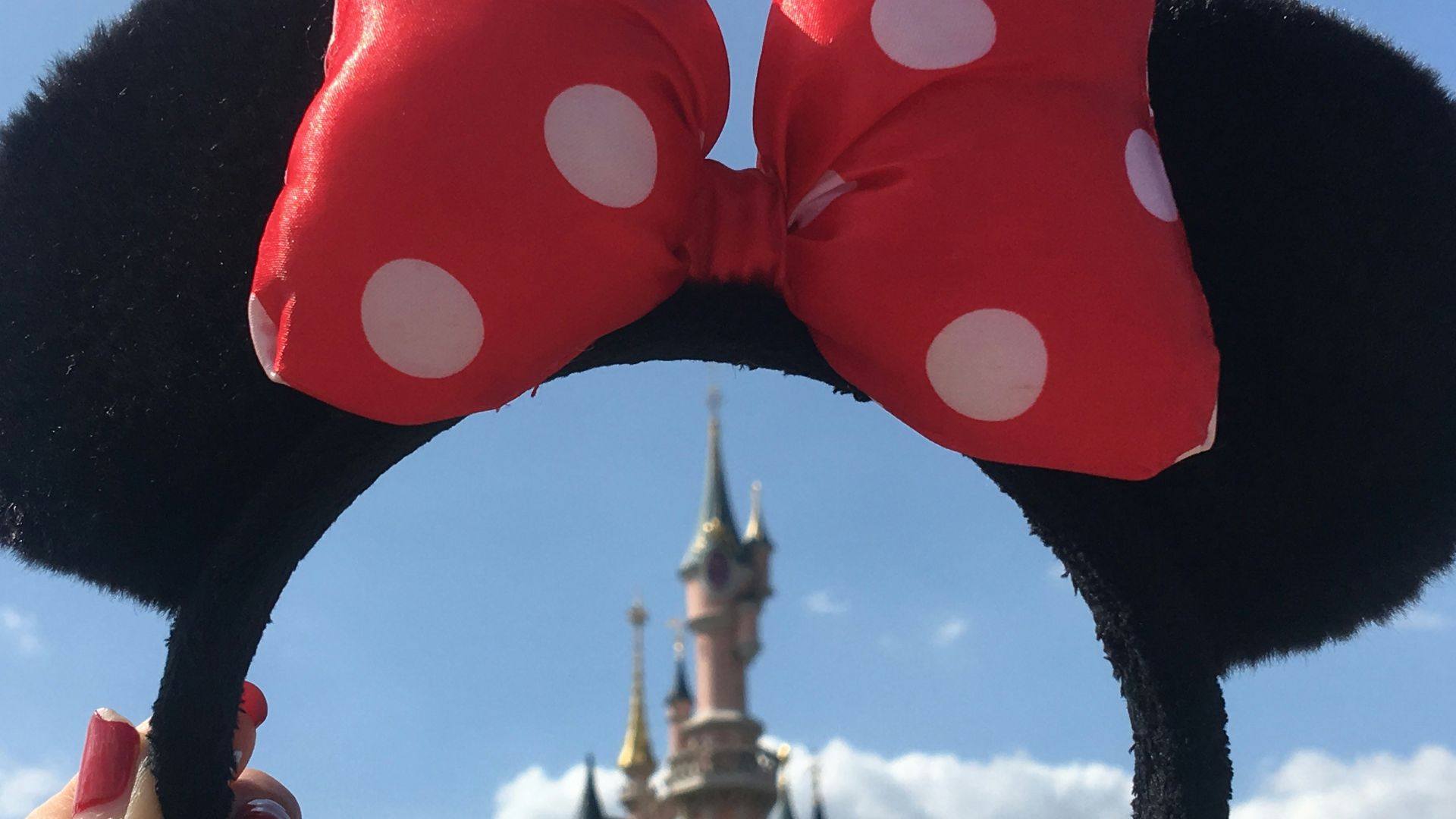 person holding Minnie Mouse headband overlooking castle