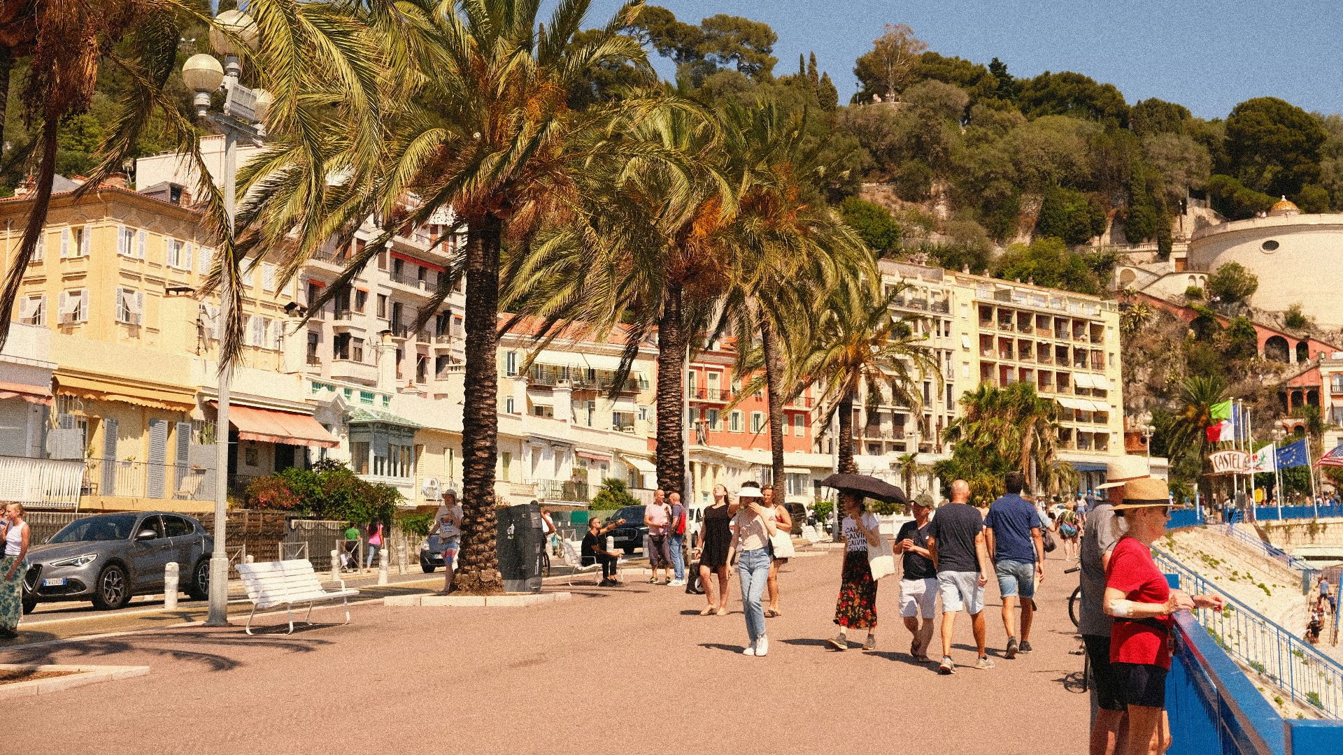 a group of people walking on a street with palm trees and buildings