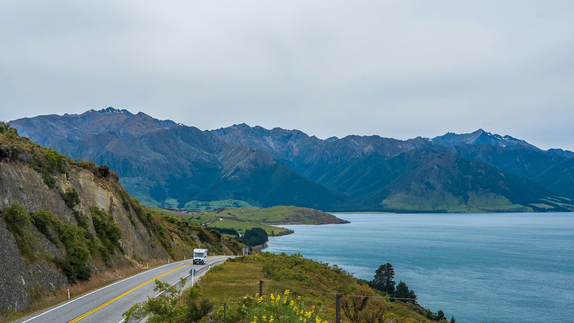 A scenic road winds beside a lake and mountains.