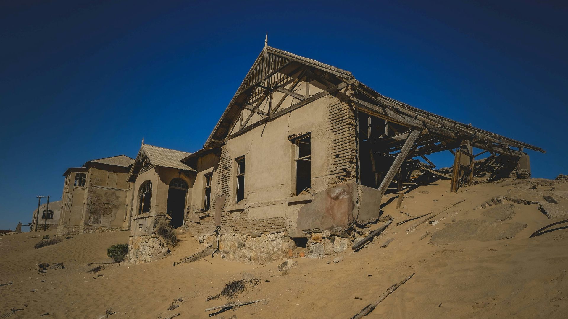 Desert sand engulfs an abandoned, weathered house.