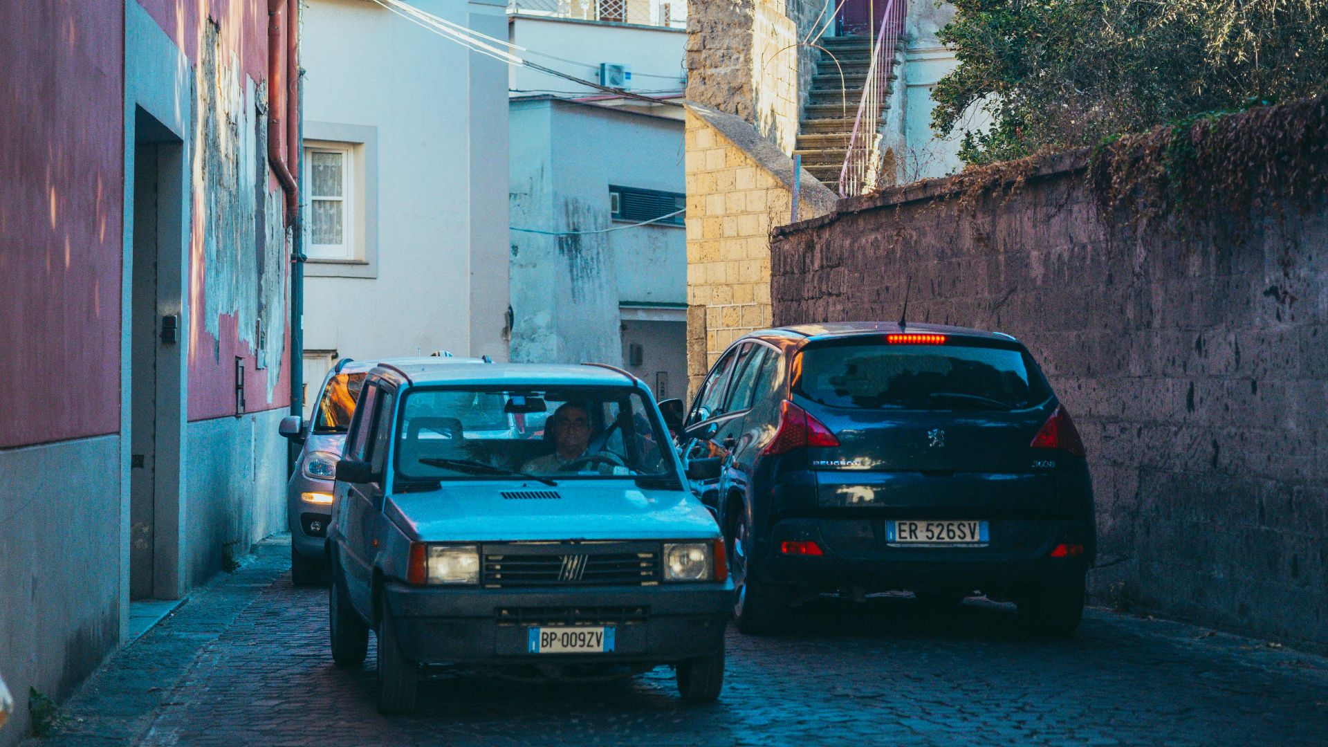 Cars driving down a narrow cobblestone street.