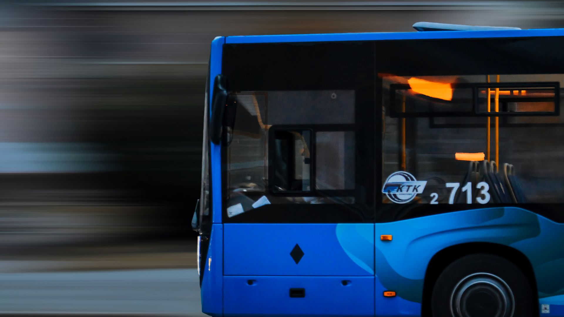 a blue bus driving down a street next to a tall building