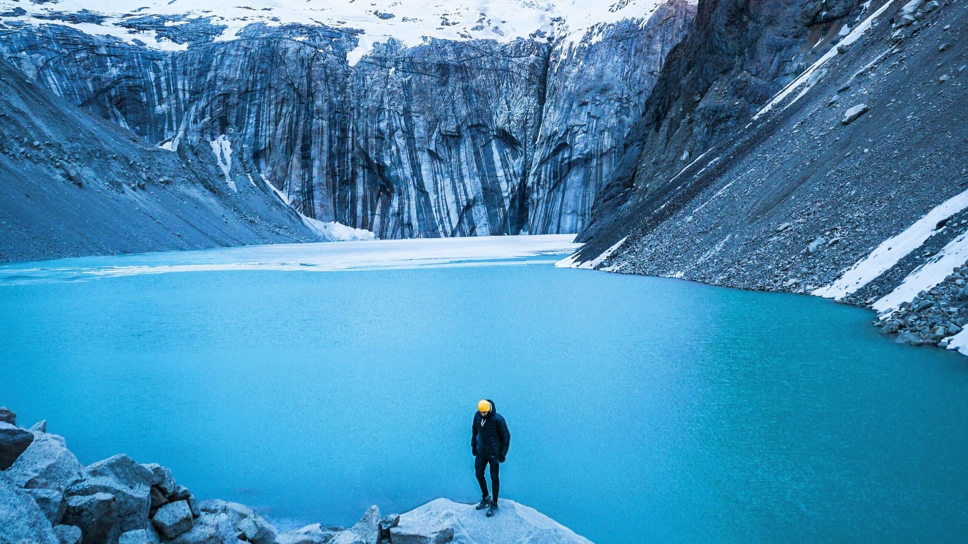 man standing on rock facing body of water and mountain