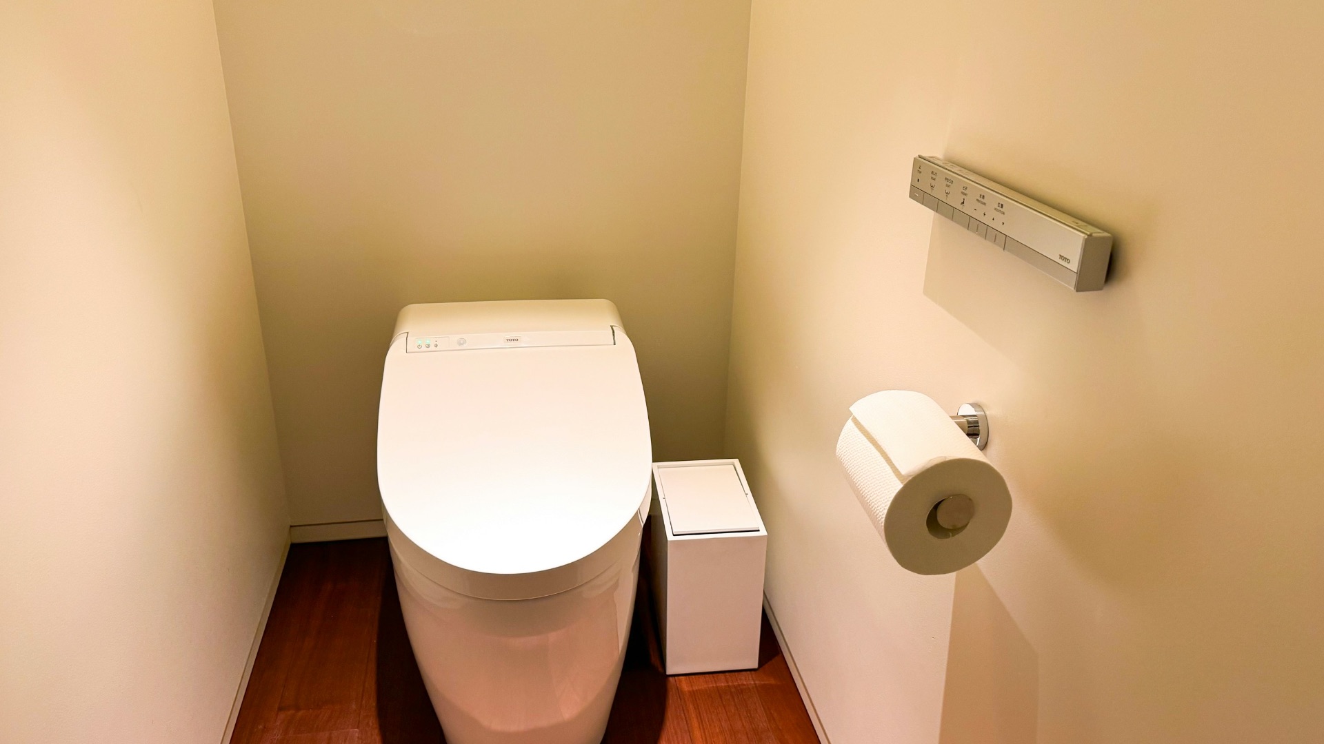 A white toilet sitting in a bathroom next to a roll of toilet paper