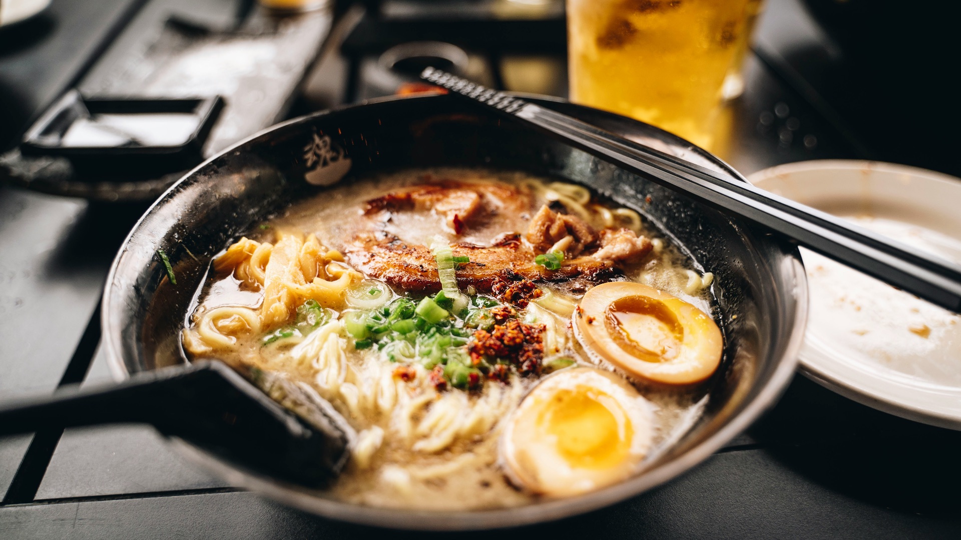 a bowl of ramen with chopsticks and a glass of beer