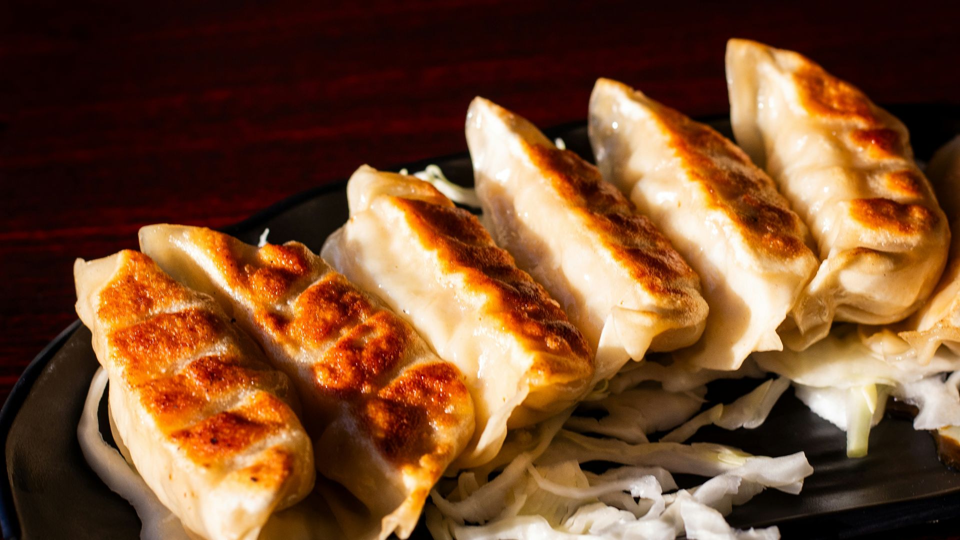 A black plate topped with dumplings on top of a wooden table