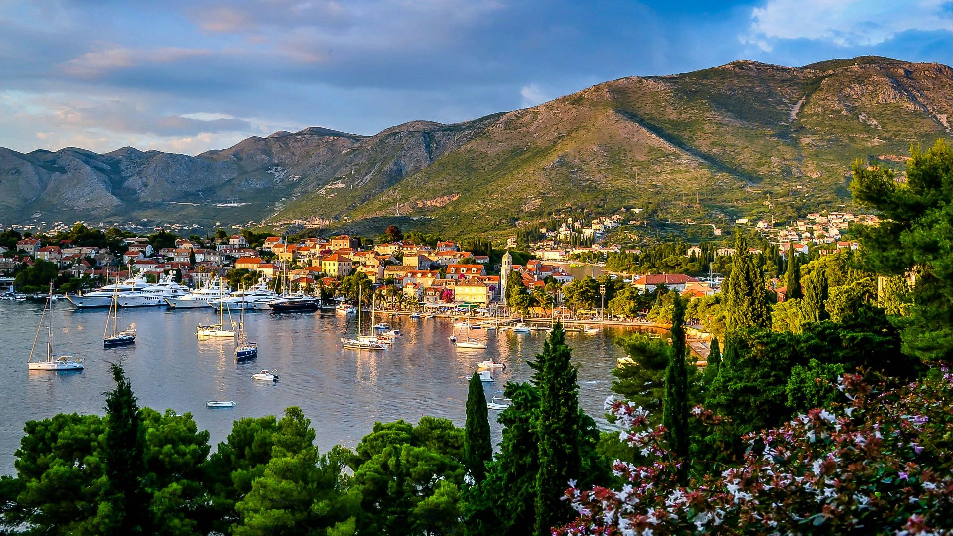 boats on body of water surrounded by trees and houses near mountain under blue and white sky at daytime