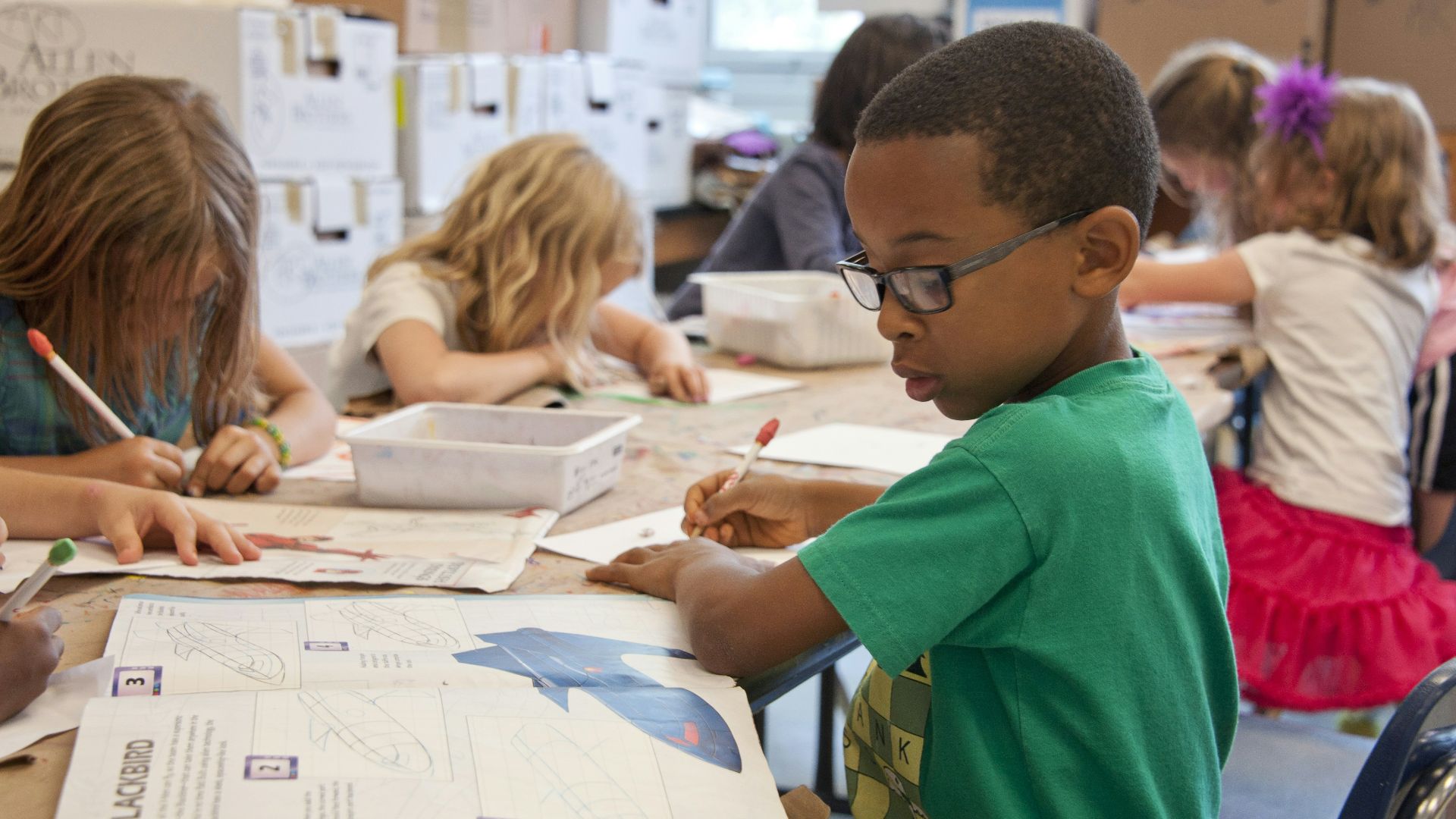 boy in green sweater writing on white paper
