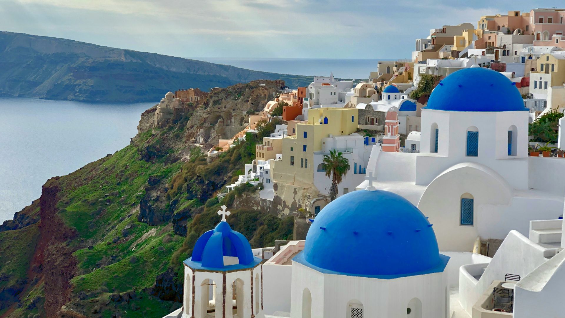 white and blue concrete building near green mountain under white clouds during daytime